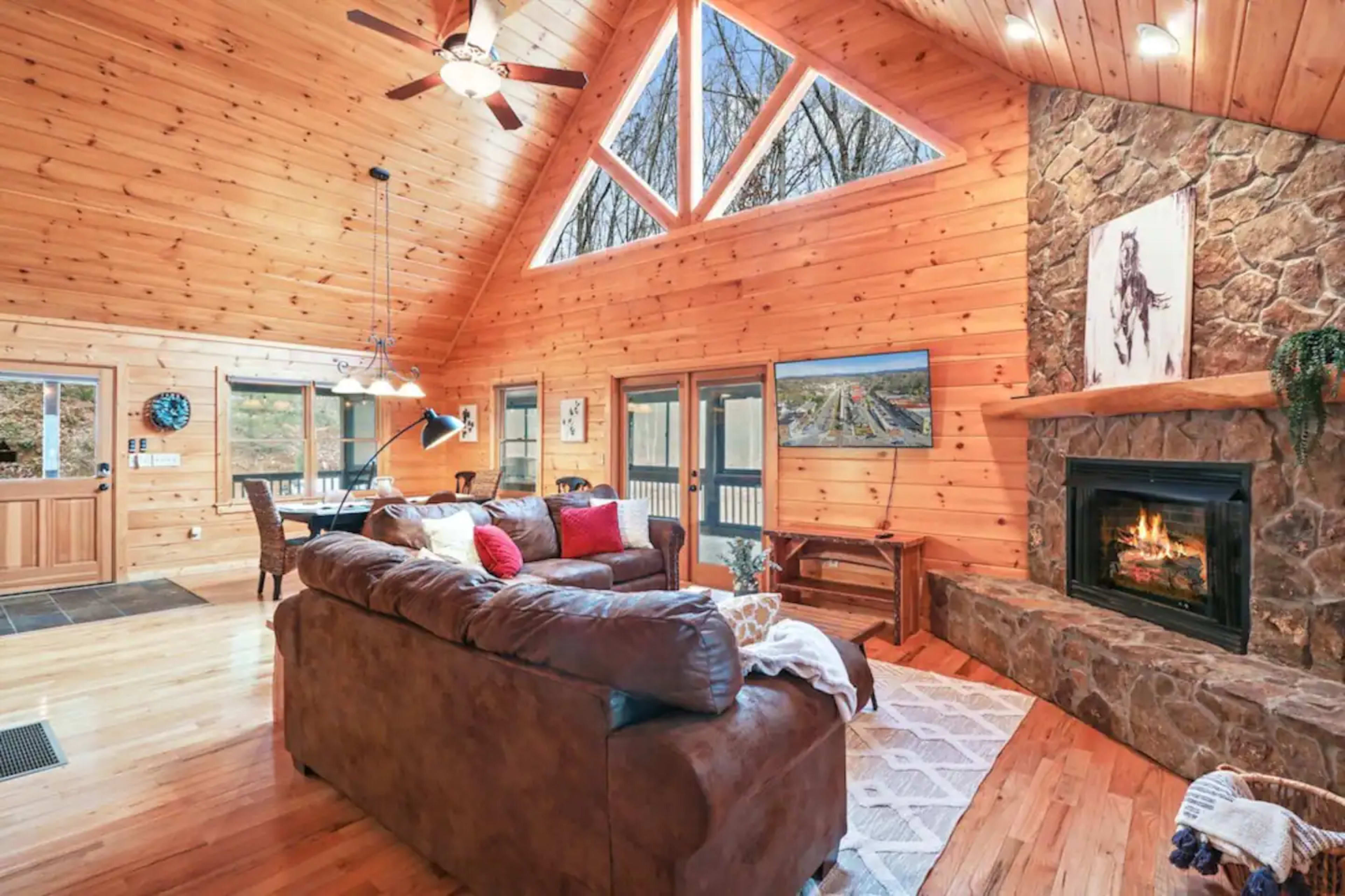 A wooden cabin interior featuring a living area with a stone fireplace, large windows, and a sectional sofa.