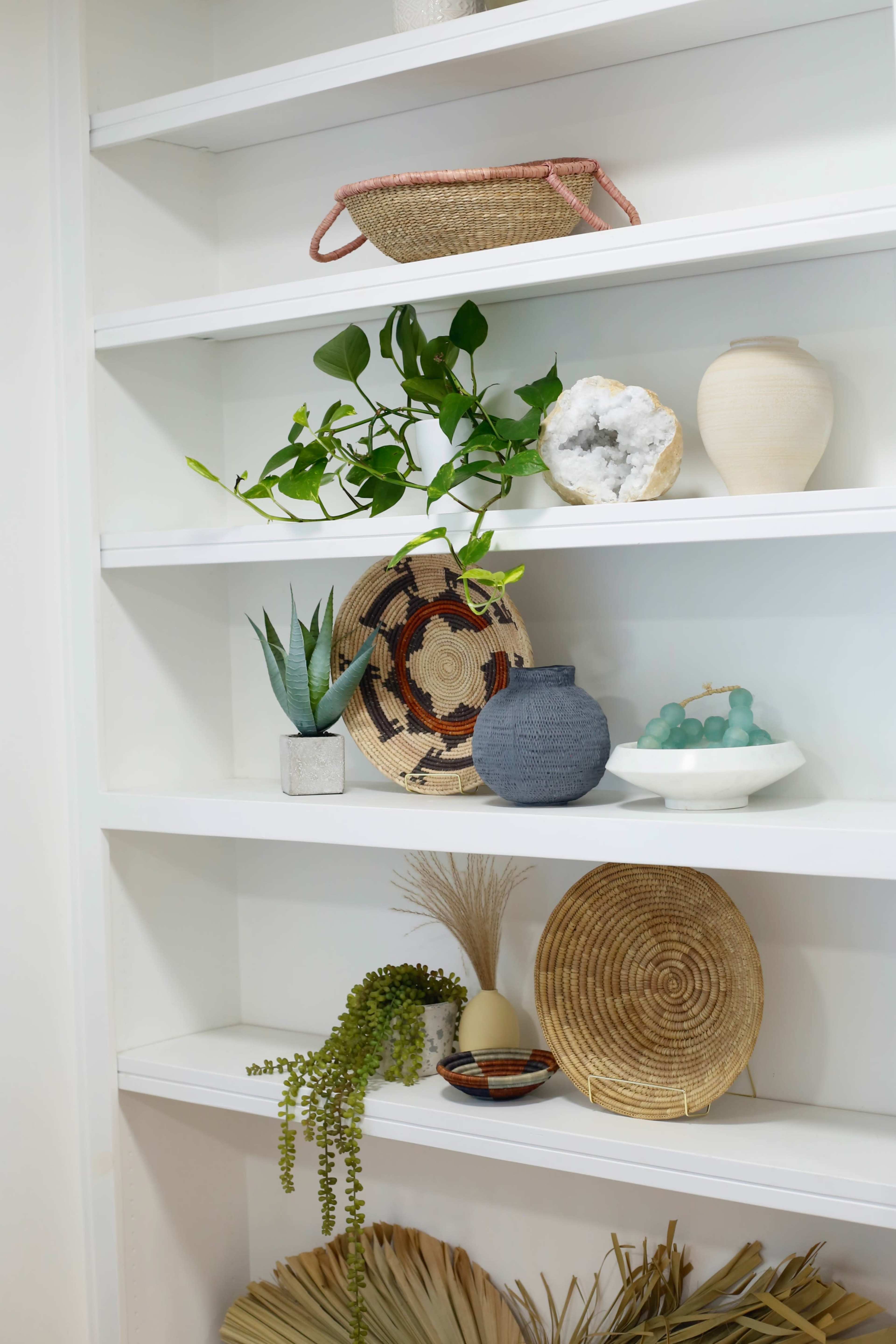 A neatly arranged shelf displays various decorative items, including plants, woven baskets, ceramics, and a textured platter.