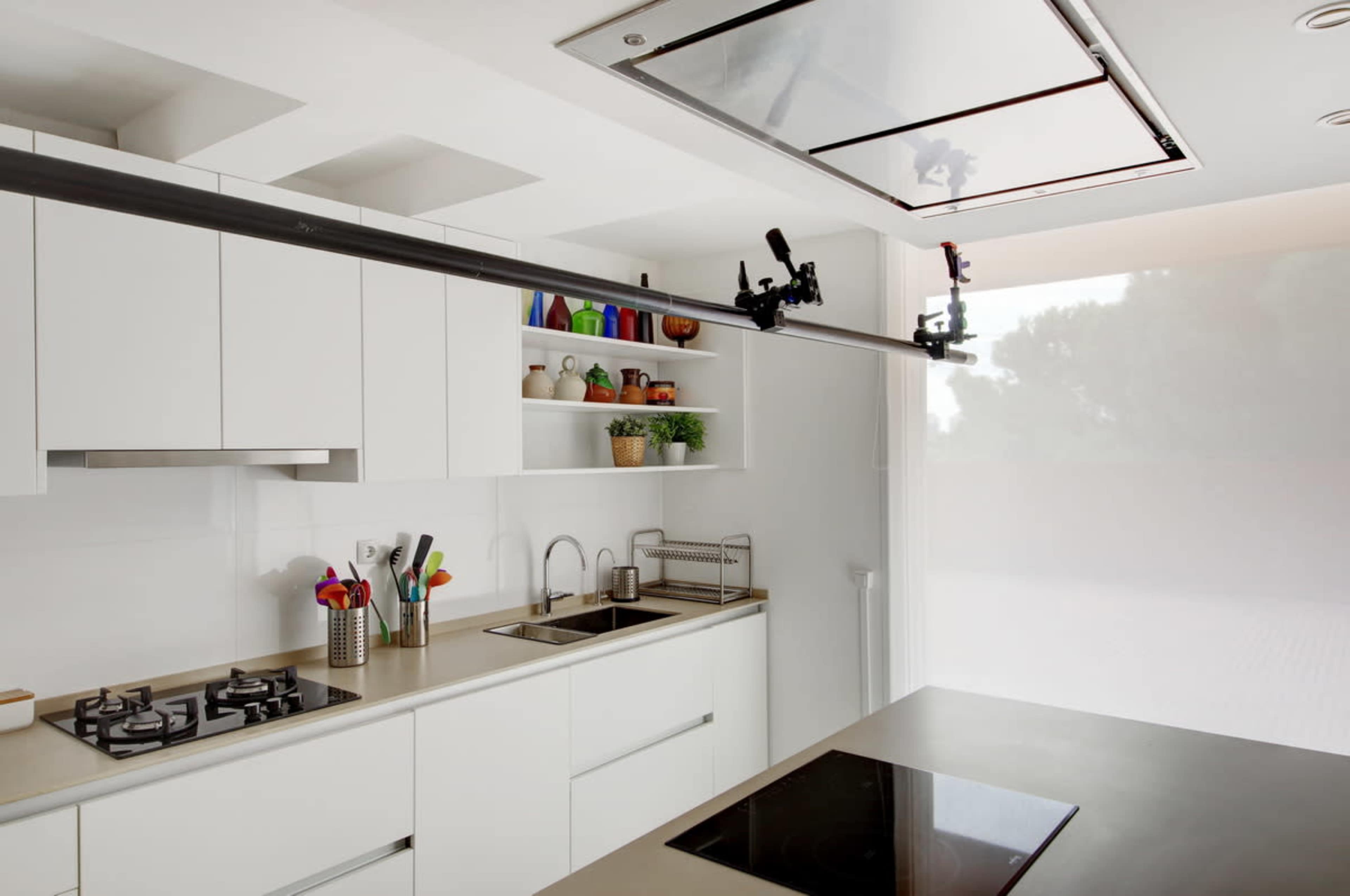 A modern kitchen features white cabinets, a stainless steel countertop, a gas stove, and a shelving unit with various kitchen items.