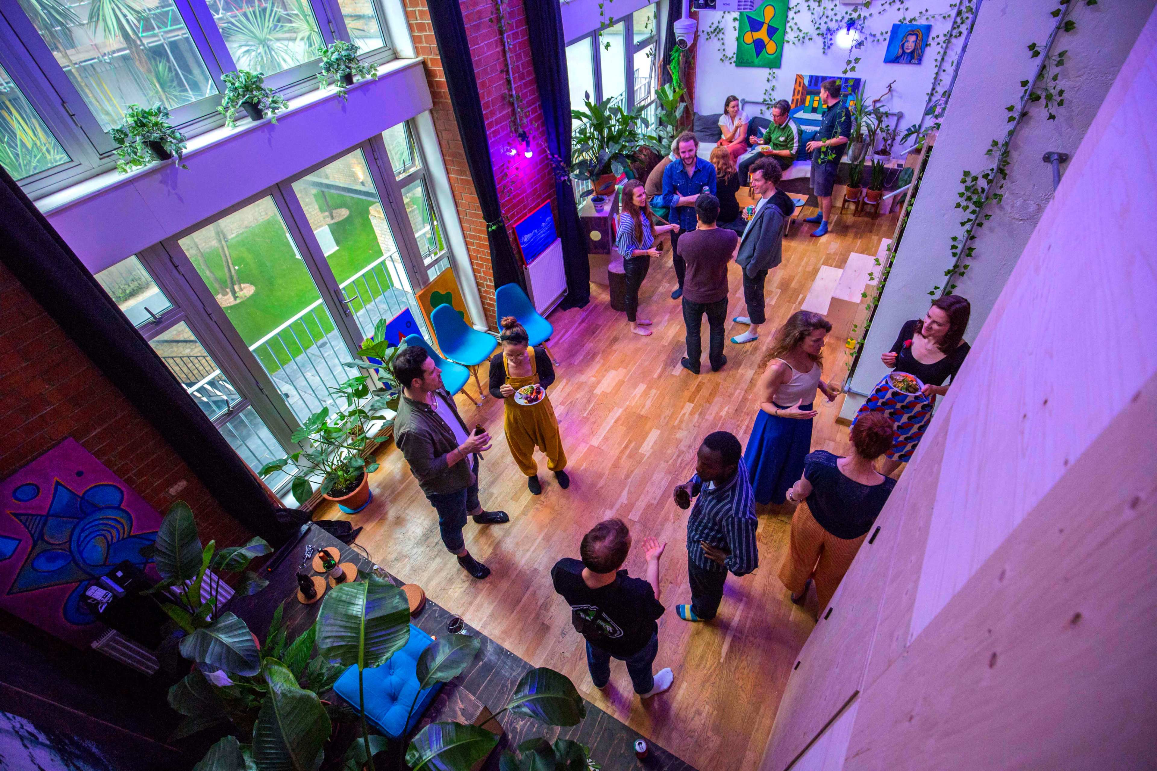 A group of people socialize in a well-lit indoor space adorned with plants and colorful artwork.