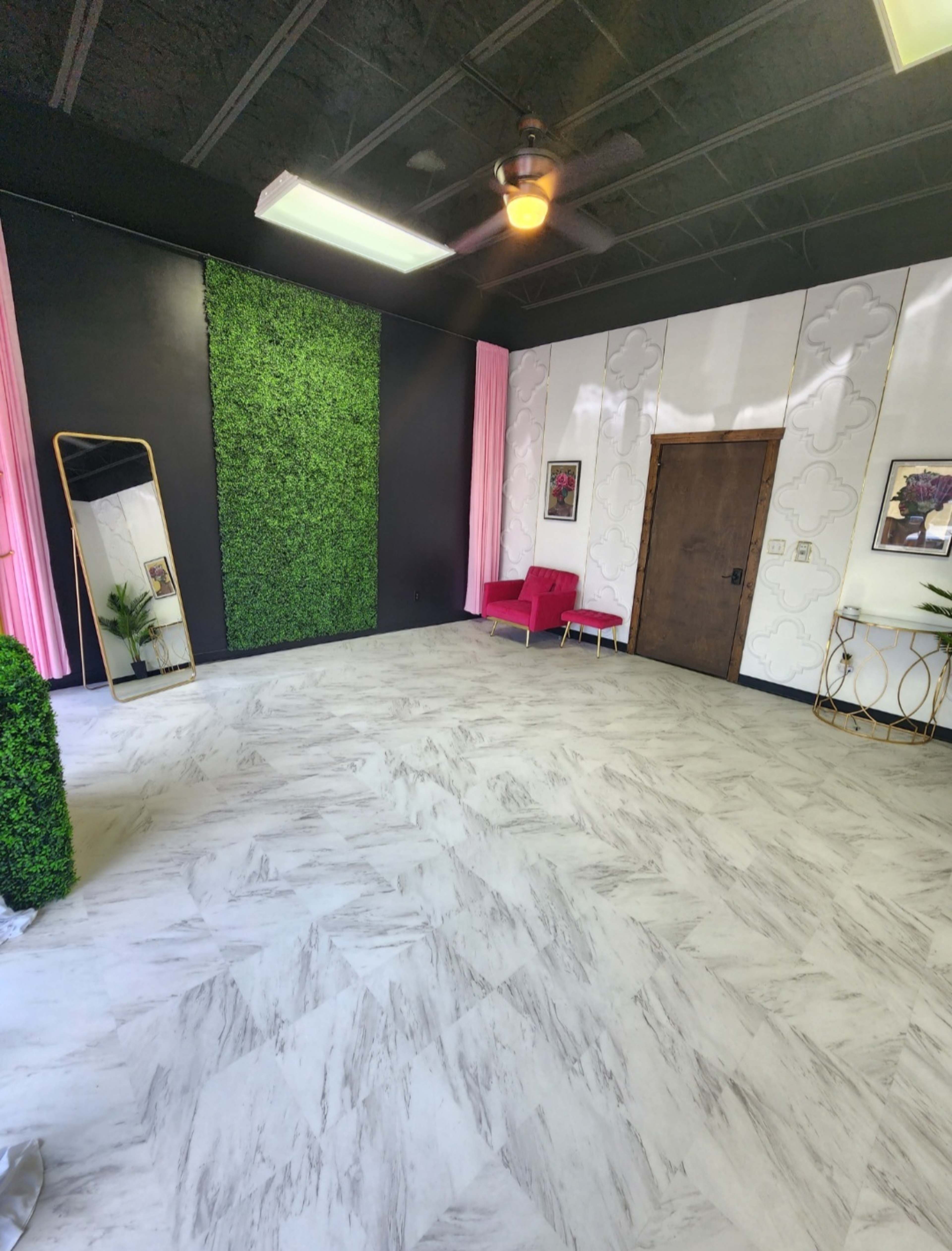 A modern room with a black accent wall, a grass wall feature, a large mirror, pink drapes, a wooden door, and a red seating area.