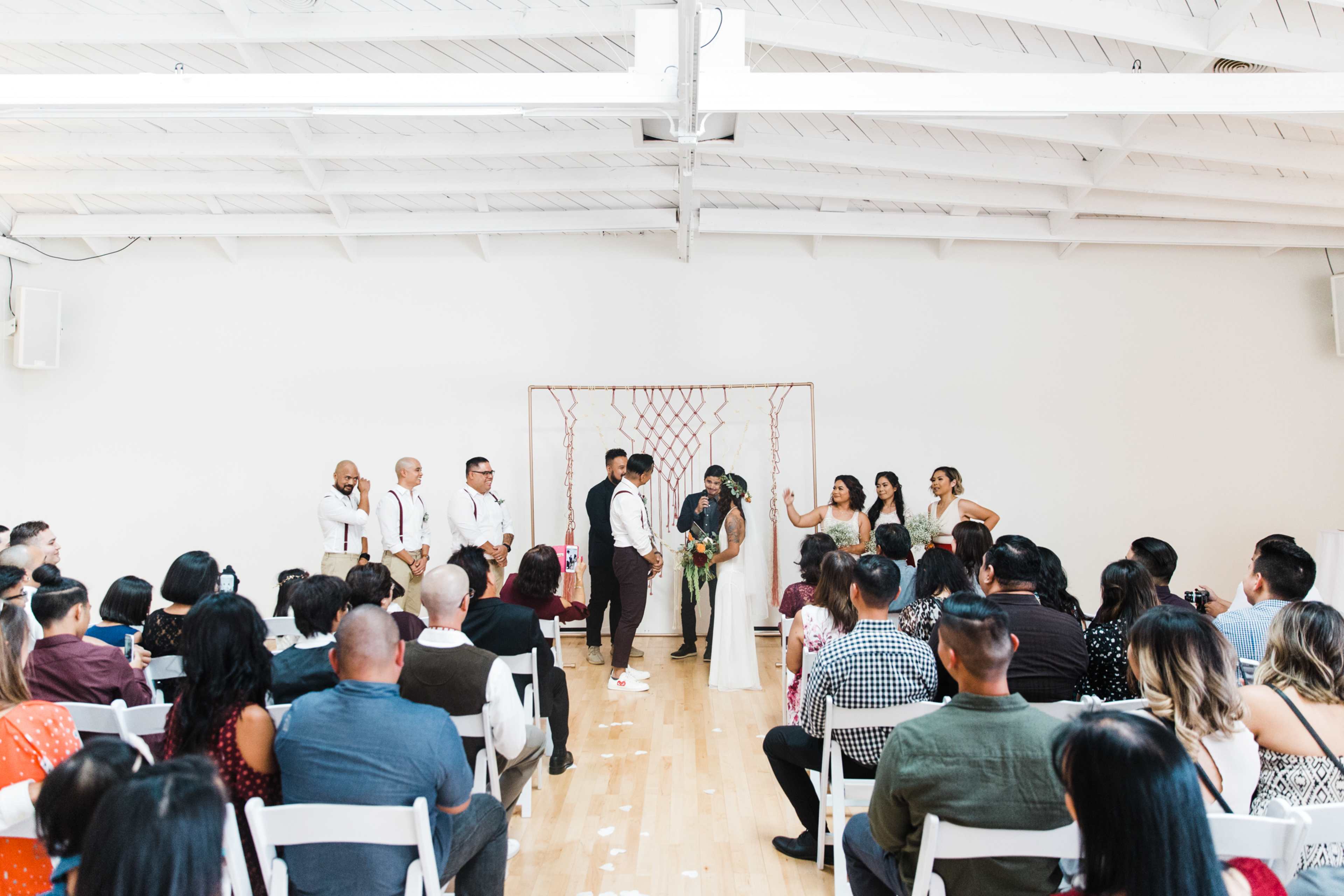 A couple stands at the altar in front of a crowd during a wedding ceremony in a well-lit indoor space.