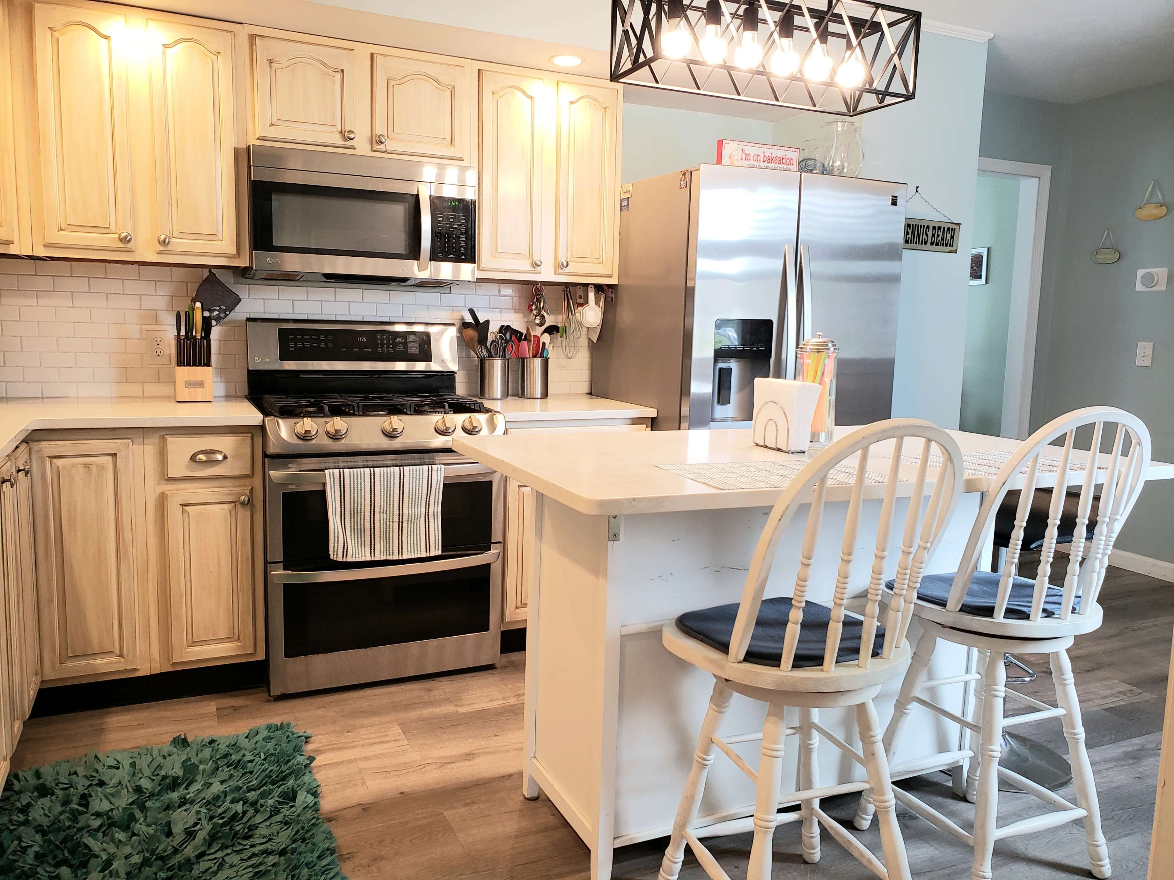 A modern kitchen with light wood cabinets, stainless steel appliances, and a central island with two white bar stools.
