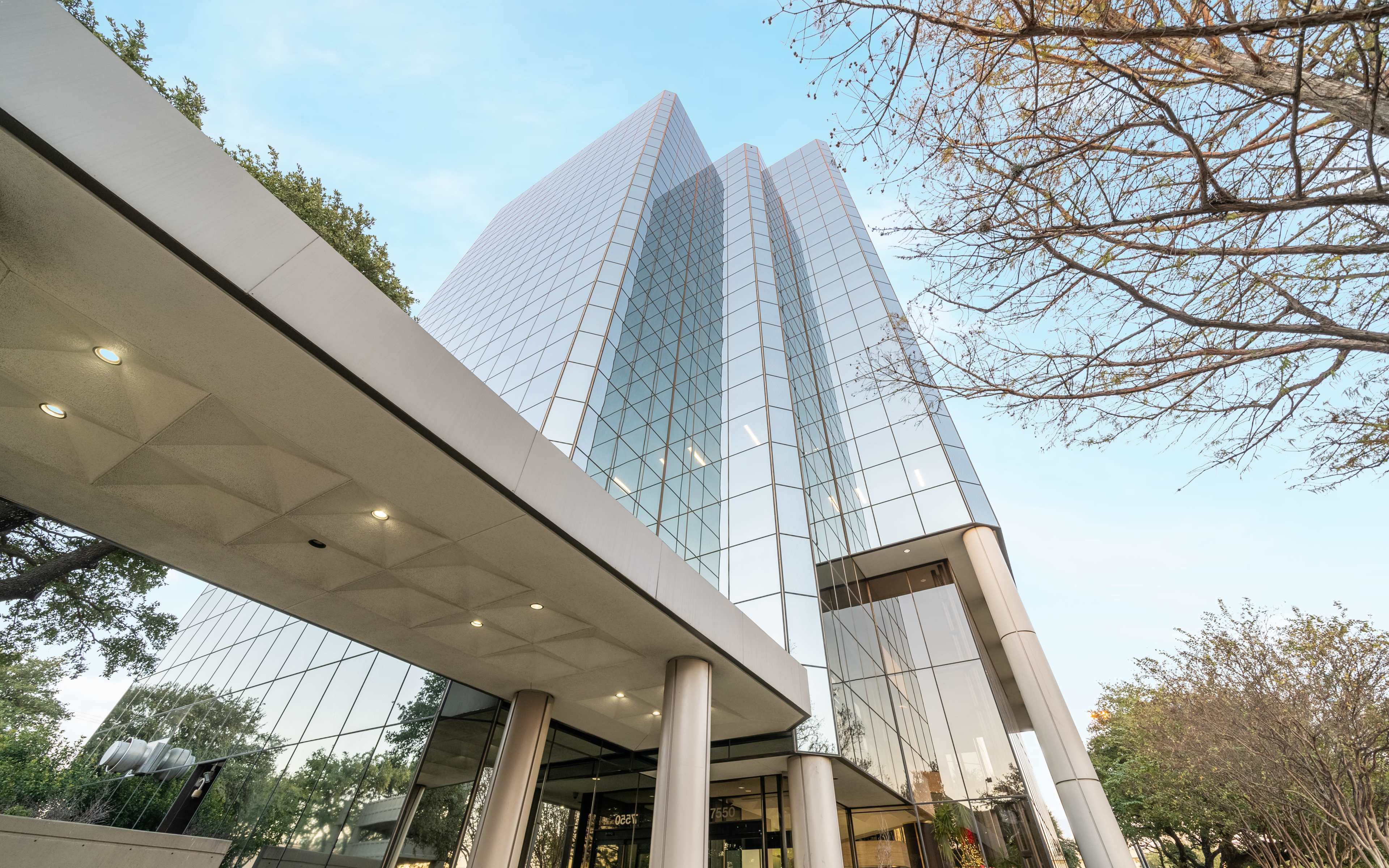 A modern glass-fronted office building with a low overhang and surrounding trees.