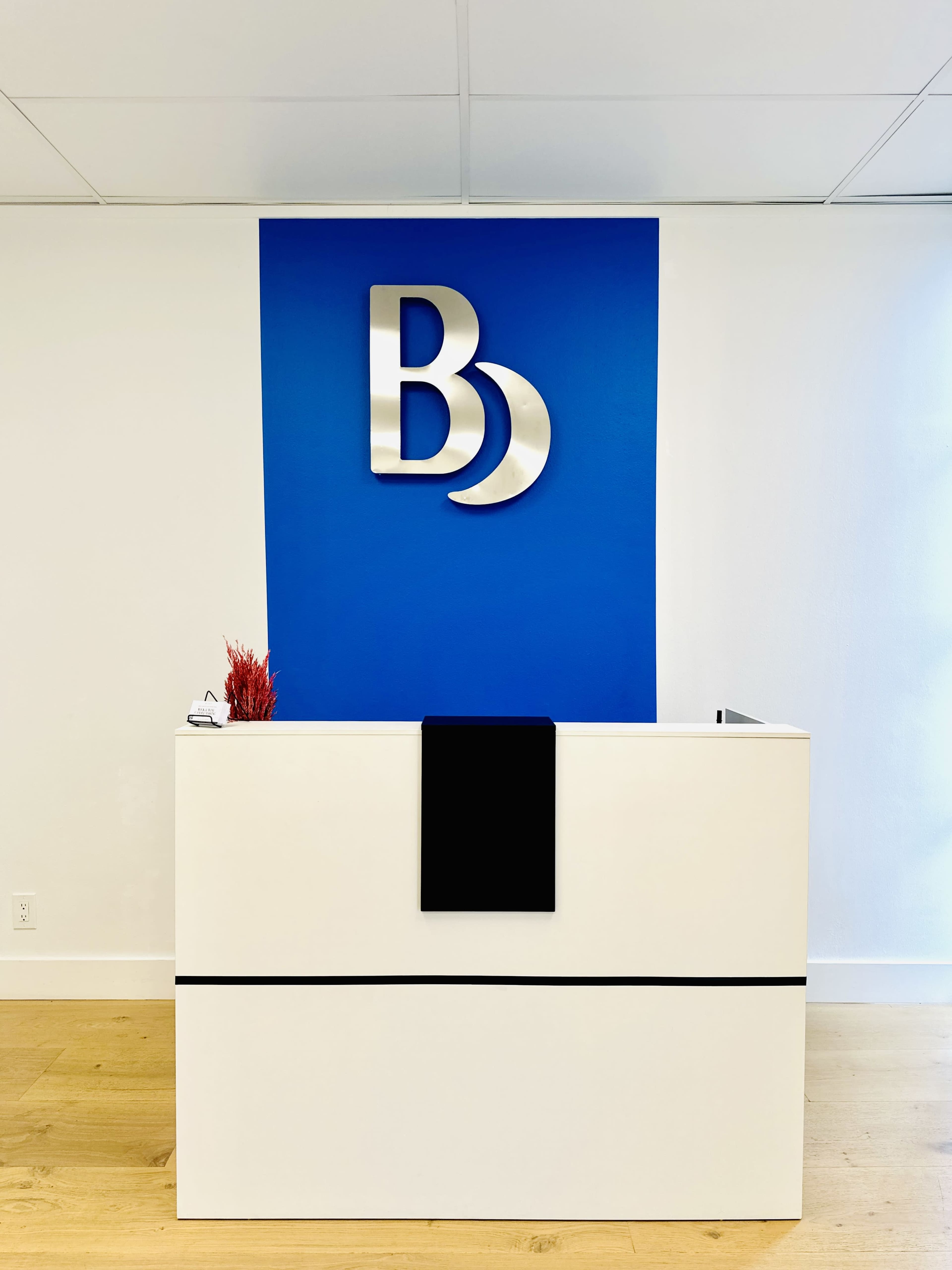 The image shows a modern reception desk with a blue wall featuring the letters "Bd" in metallic finish.