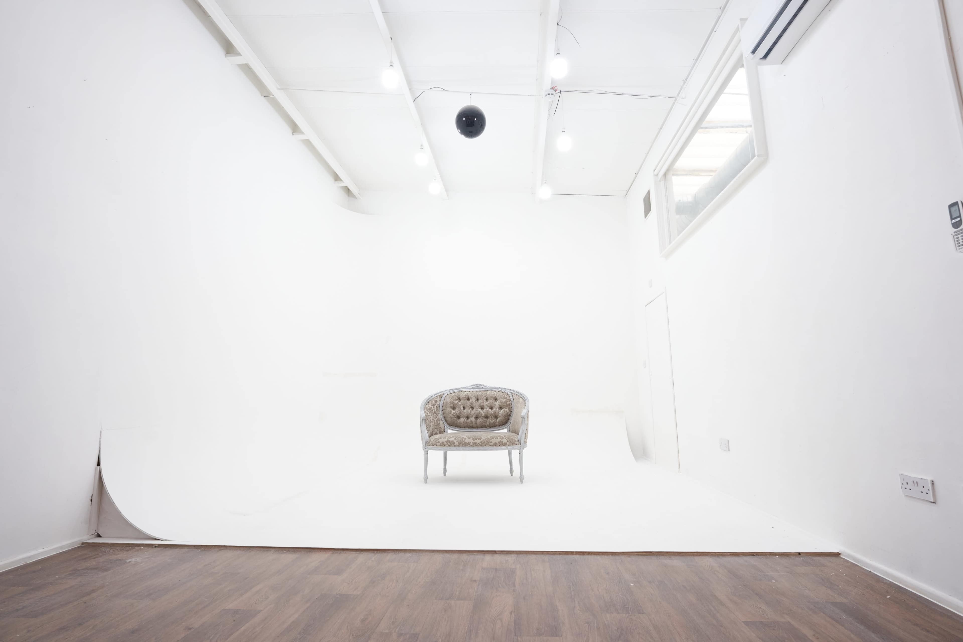 A minimalist studio space with a single tufted chair on a white backdrop and overhead lighting.