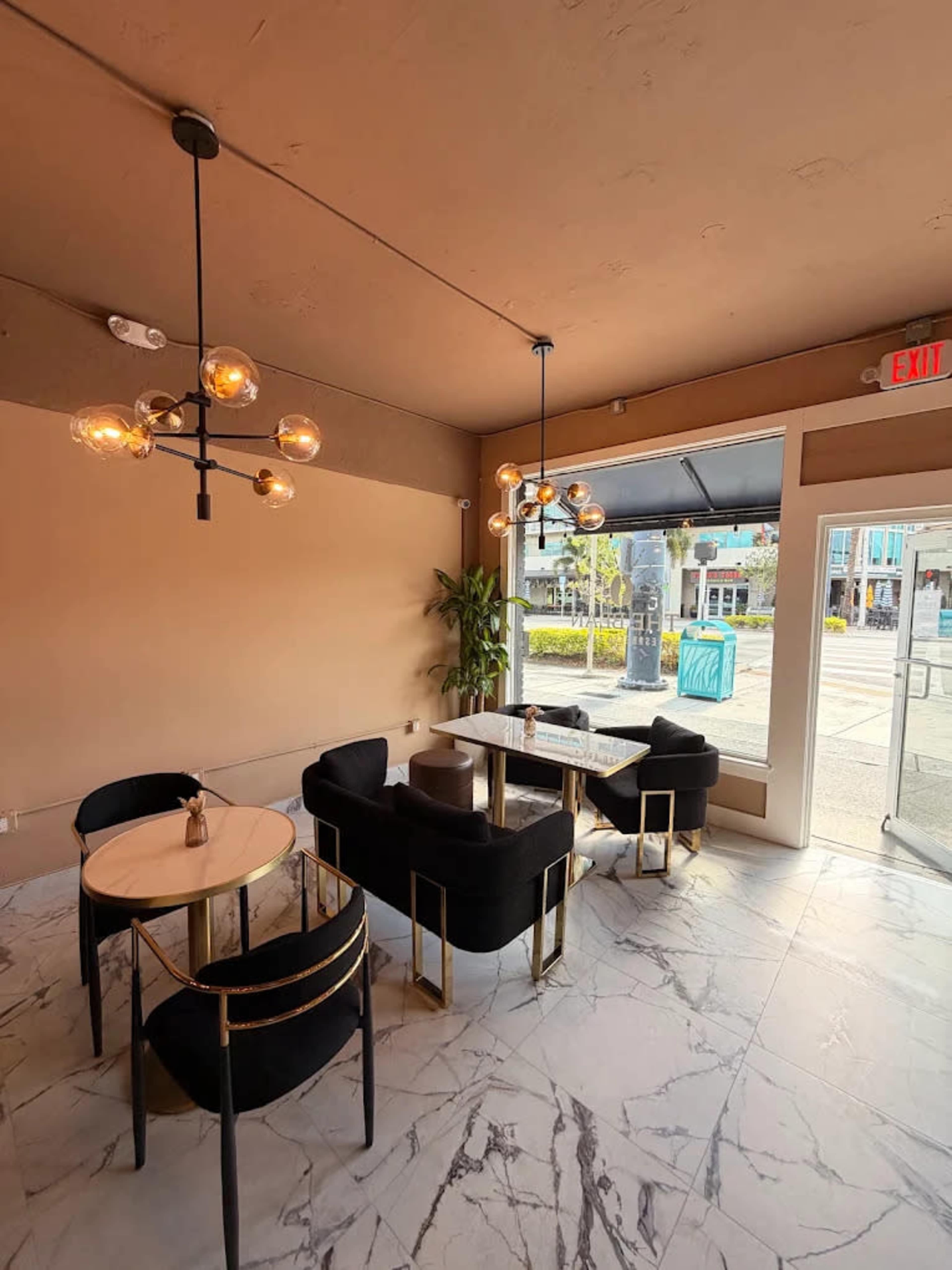 The image shows a modern cafe interior with black seating, round tables, and large windows facing a street.