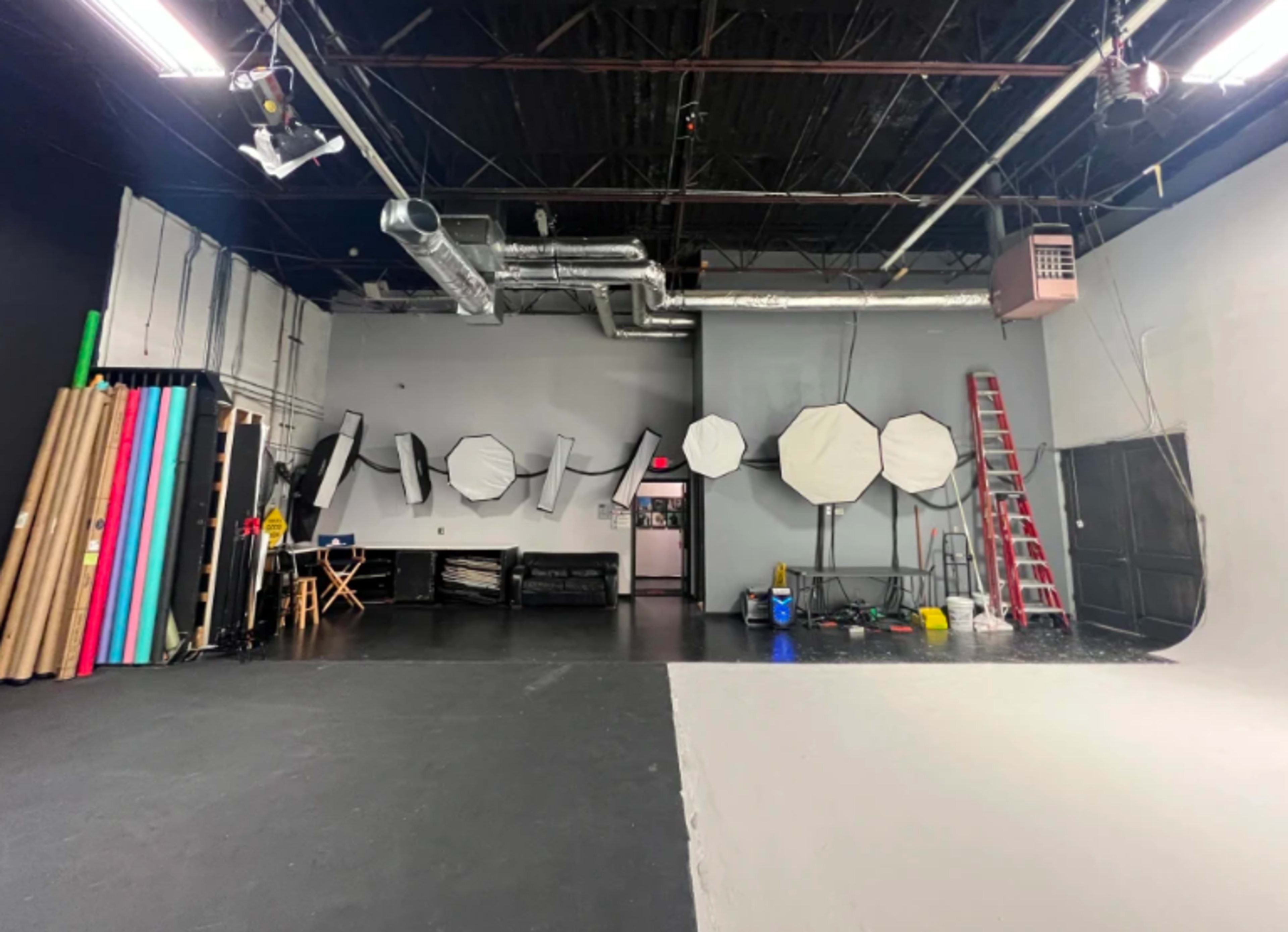 The image shows a photography studio with various lighting equipment and backdrops arranged along the walls.