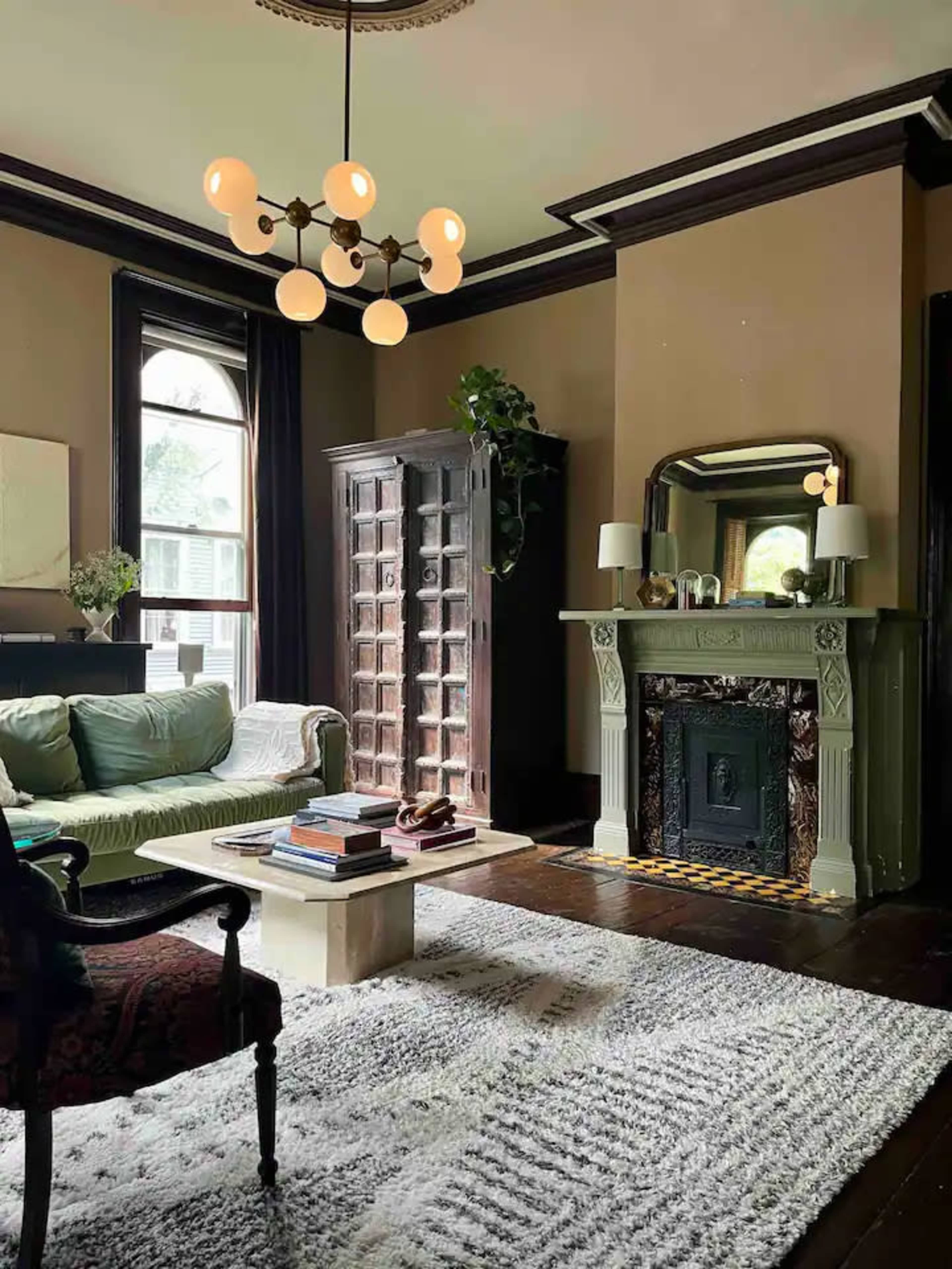 A living room with a green sofa, a wooden bookcase, a fireplace with a decorative mantel, and a light fixture hanging from the ceiling.