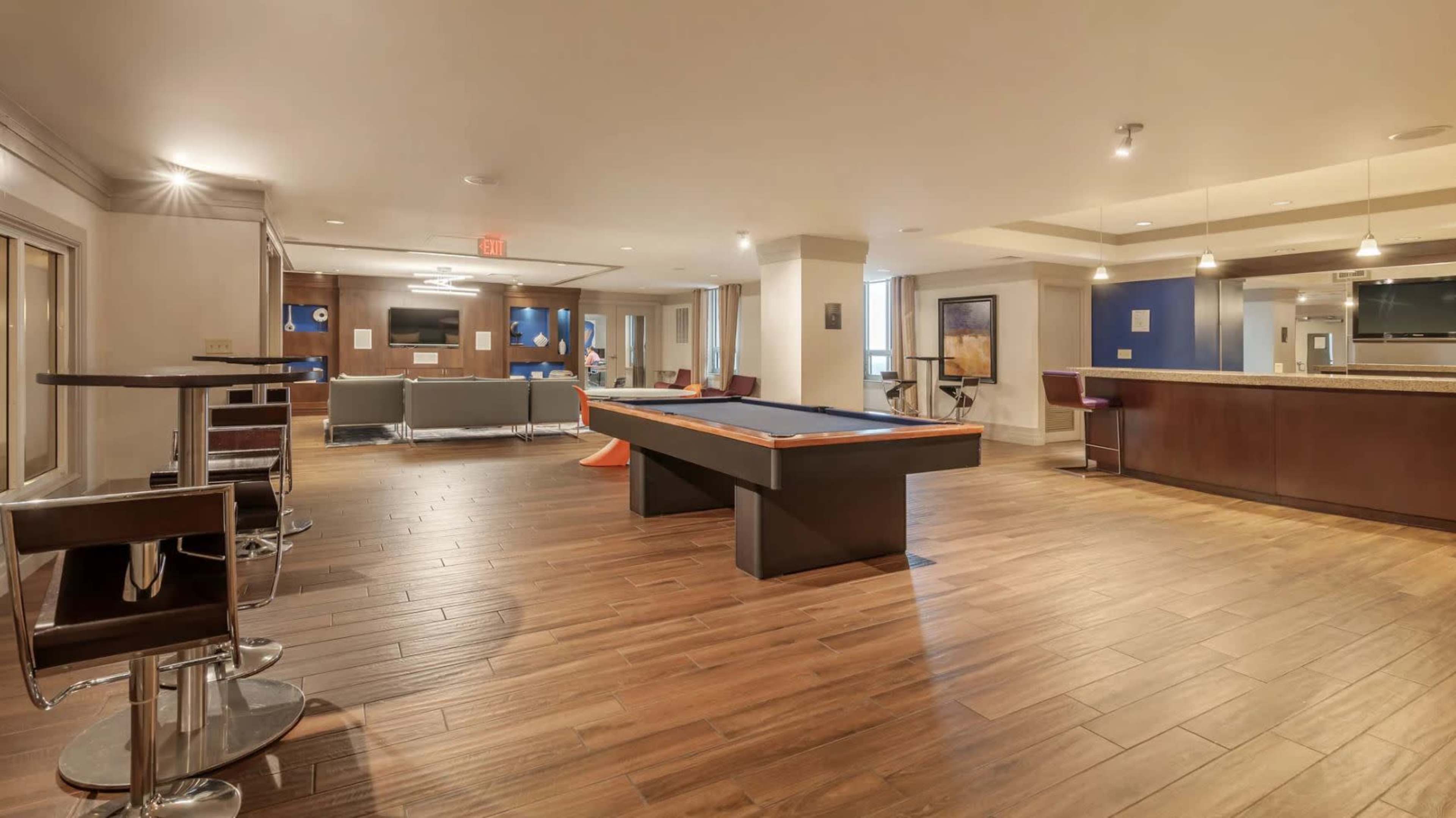 A spacious lounge area with a pool table, bar seats, and a seating arrangement in a modern environment.