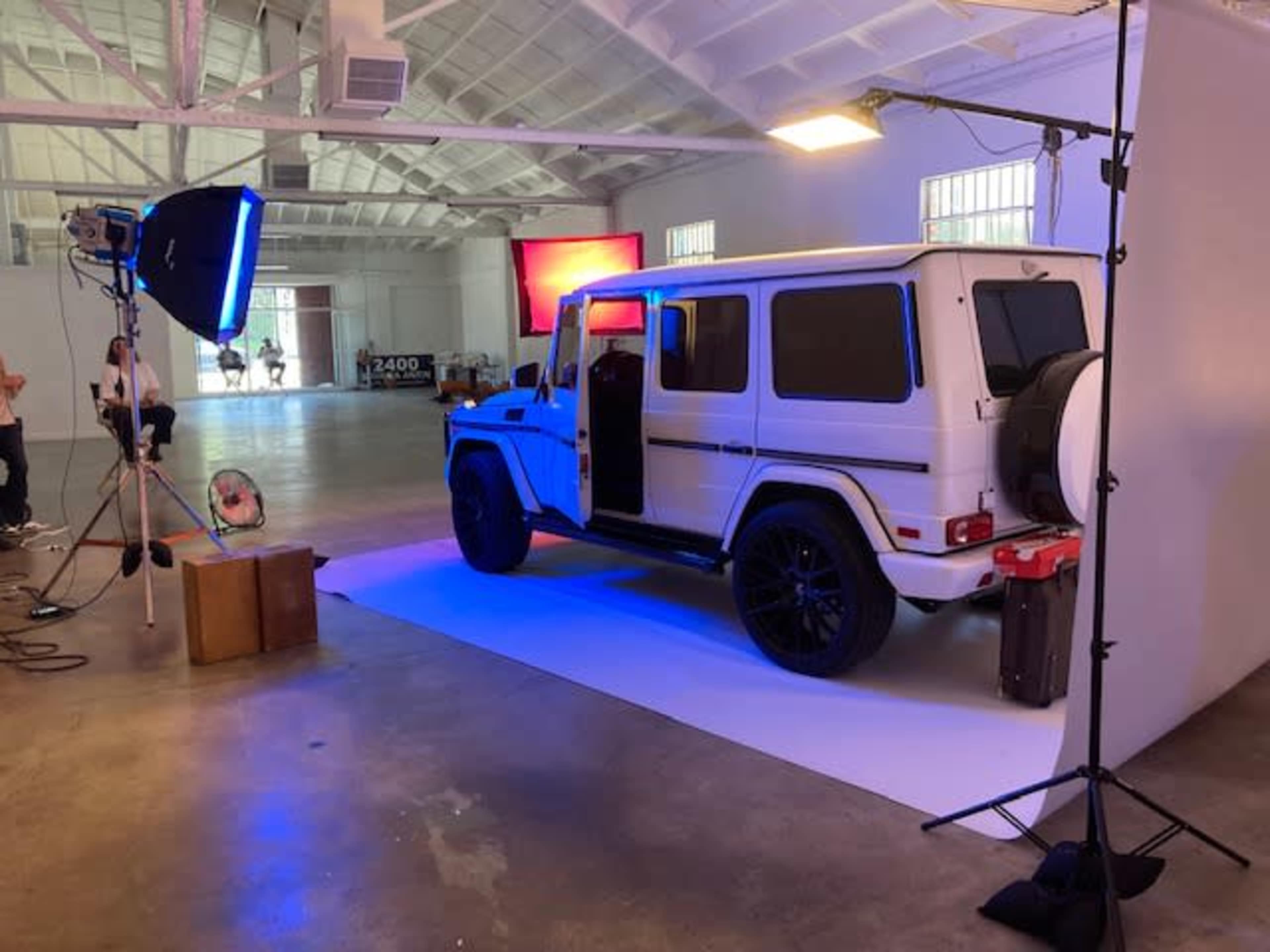 A white SUV is positioned in a spacious, well-lit studio with photography equipment set up nearby.