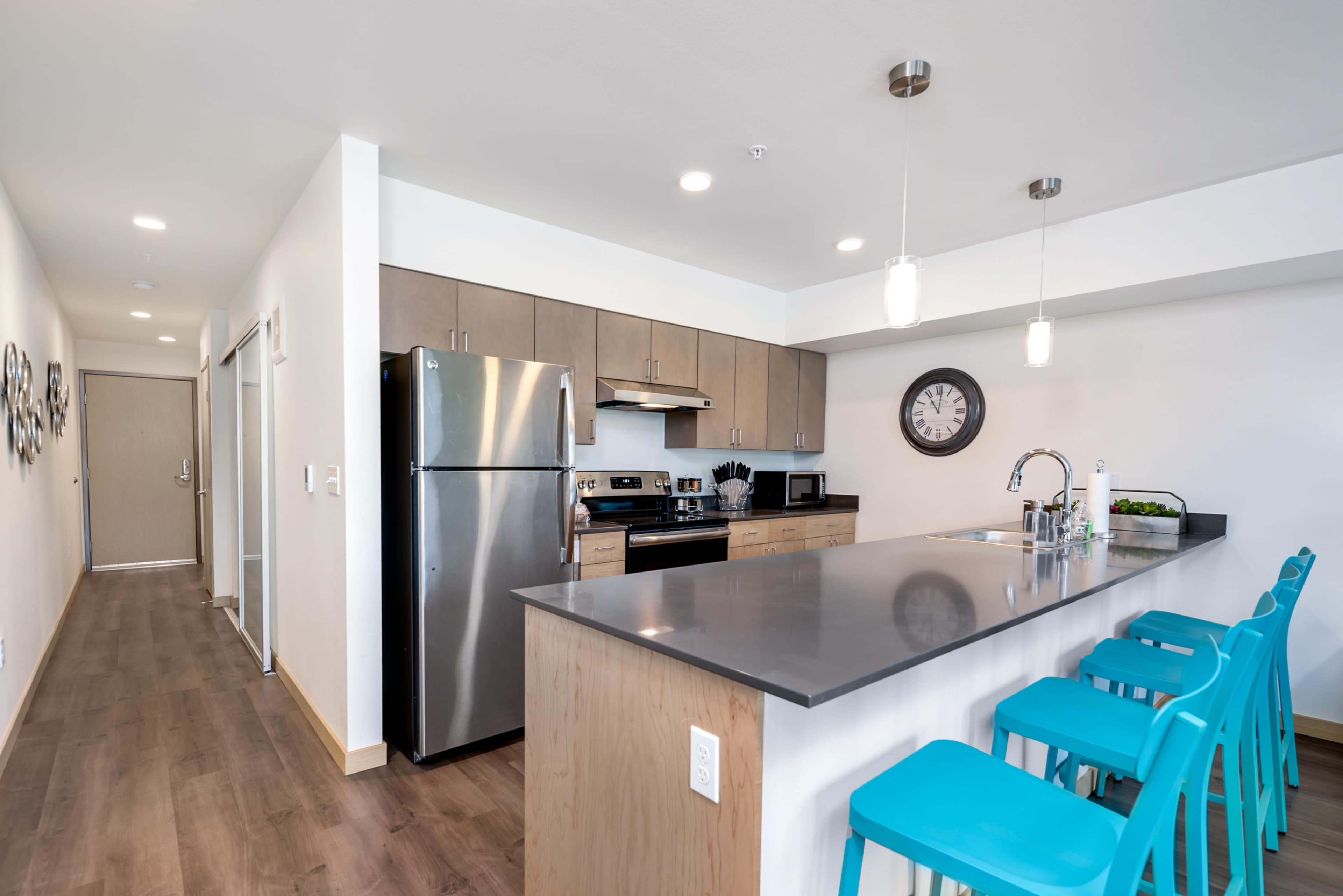 A modern kitchen with stainless steel appliances and a long island featuring turquoise bar stools.