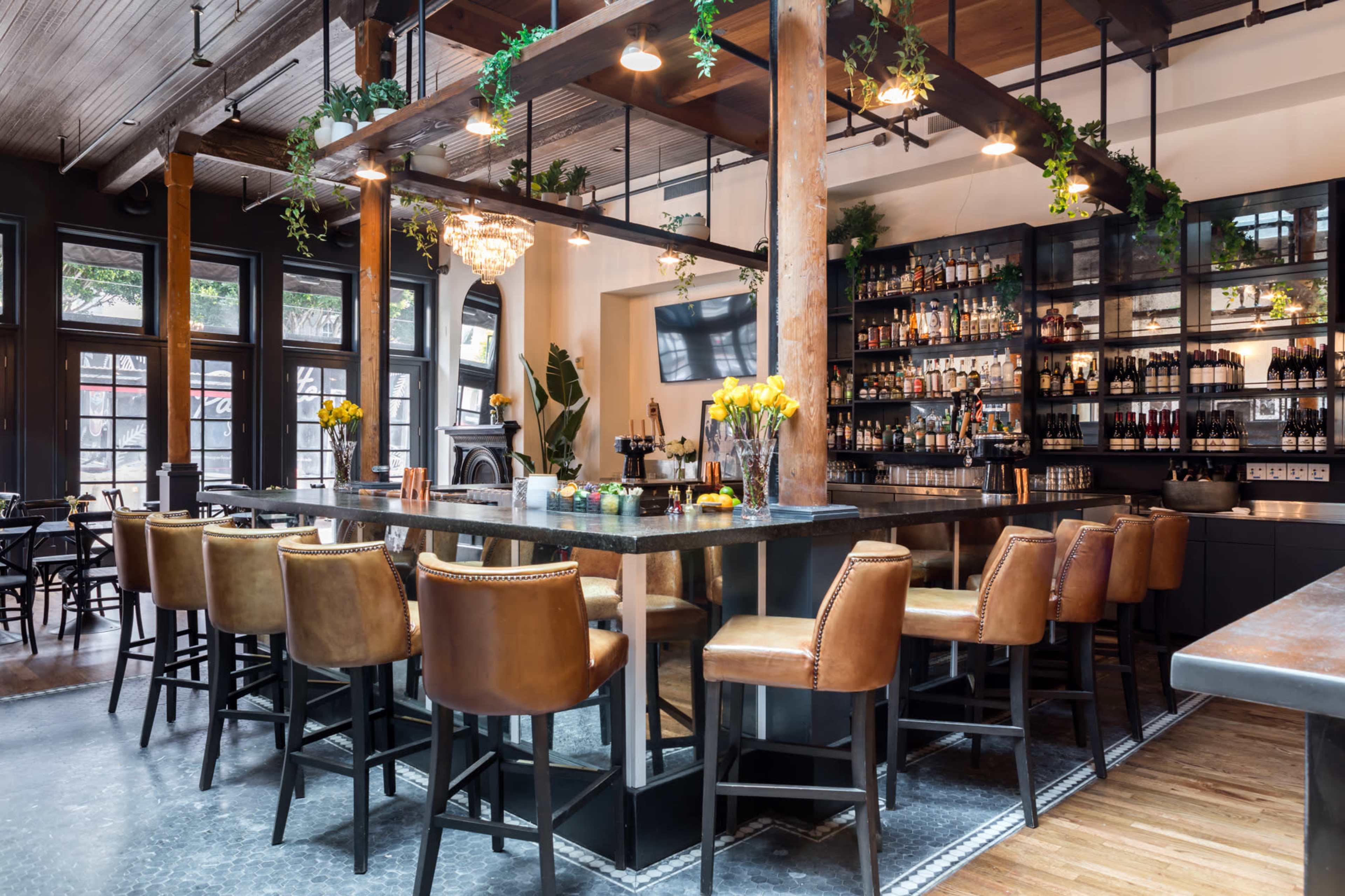 The image showcases a stylish bar area with leather seating, wooden beams, and shelves lined with various bottles and glassware.