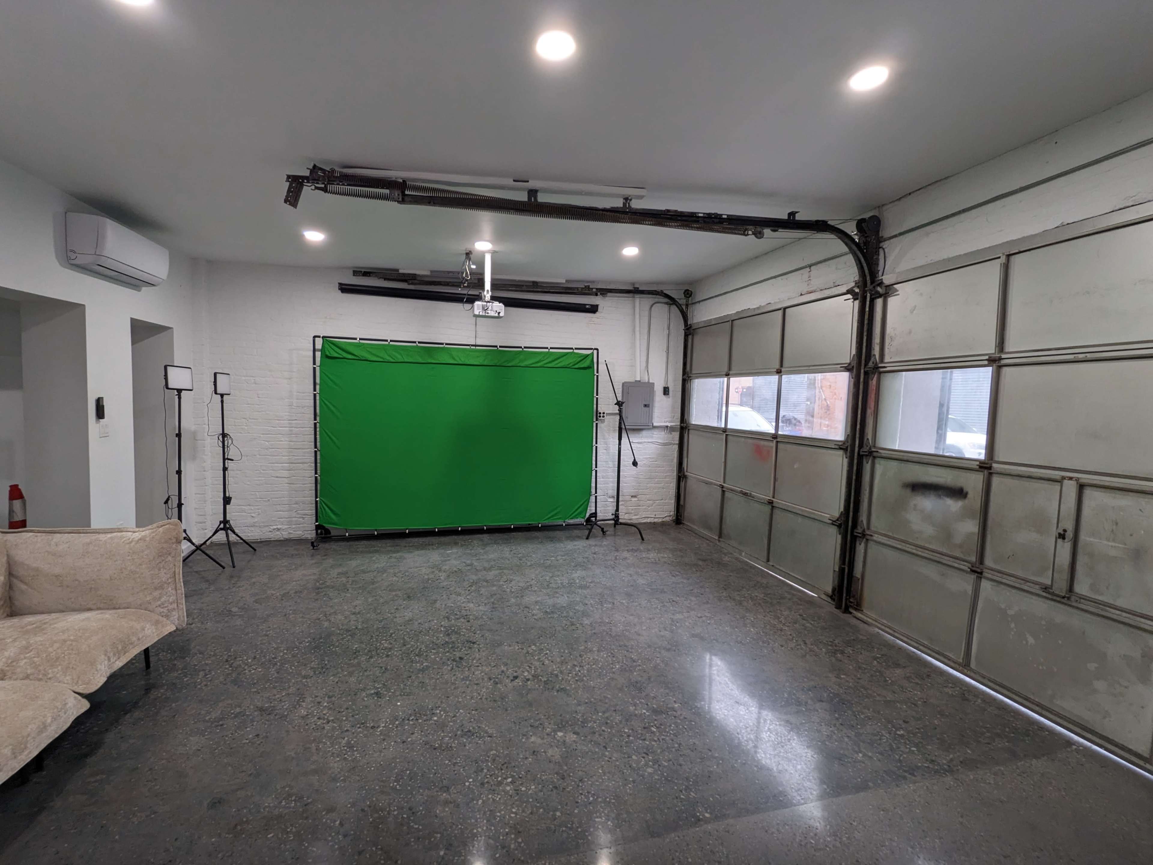 The image shows a large, empty garage space with a green screen setup and softbox lights positioned on either side.