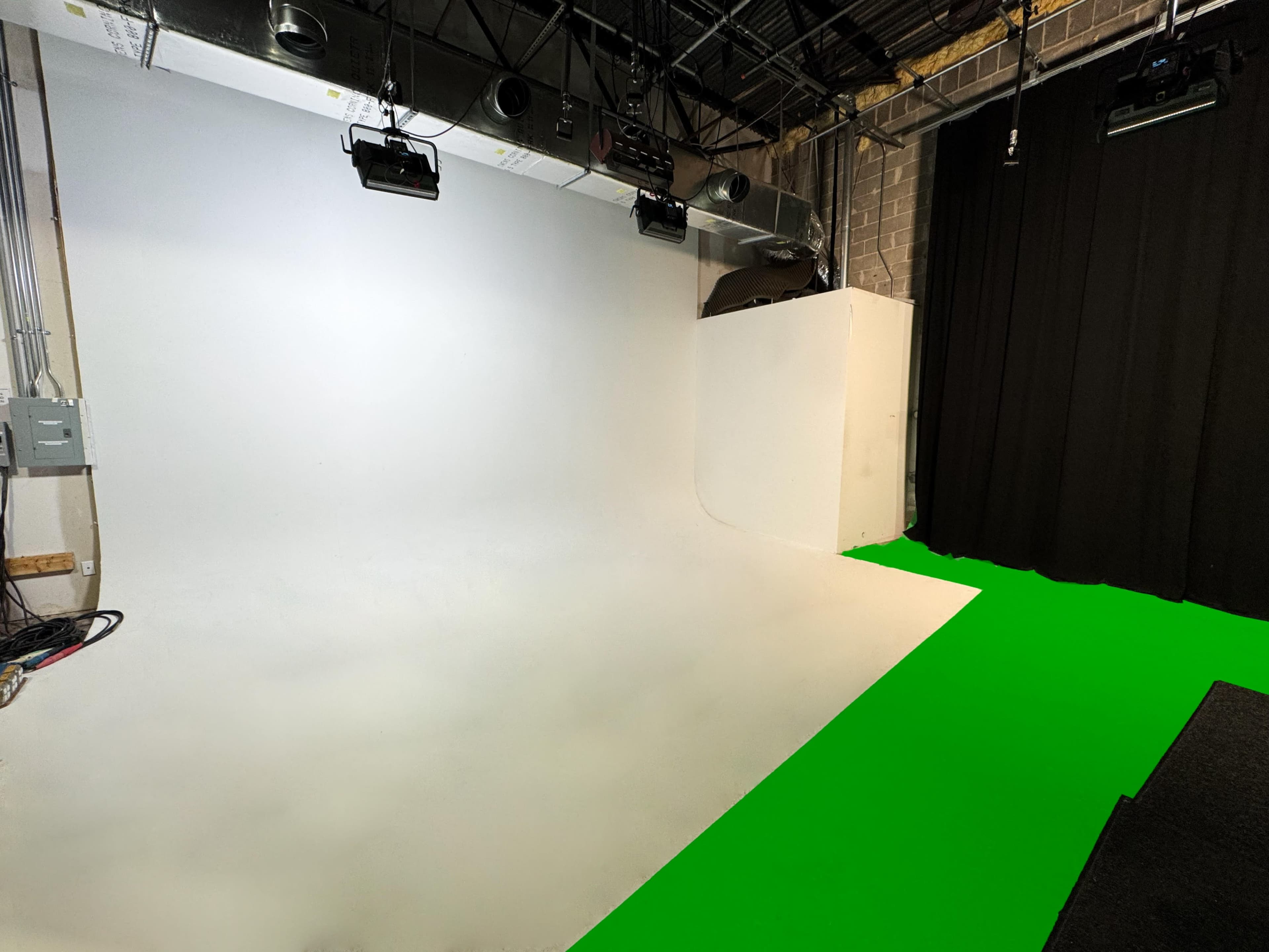 The image shows a studio space featuring a white backdrop with a seamless curve, a green floor area, and black curtains along one side.