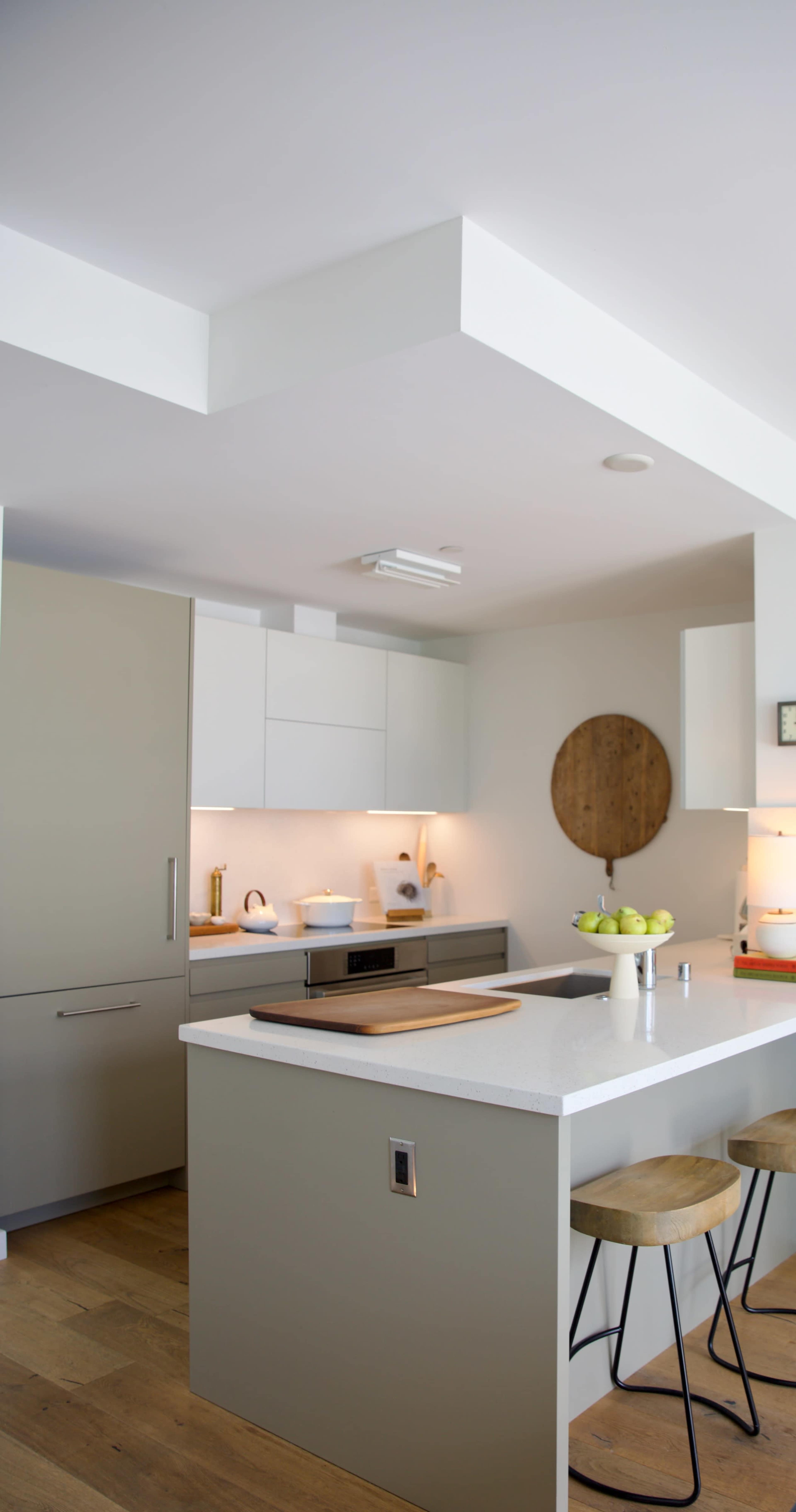A modern kitchen with a central island, light grey cabinetry, and illuminated shelves displaying kitchen items.
