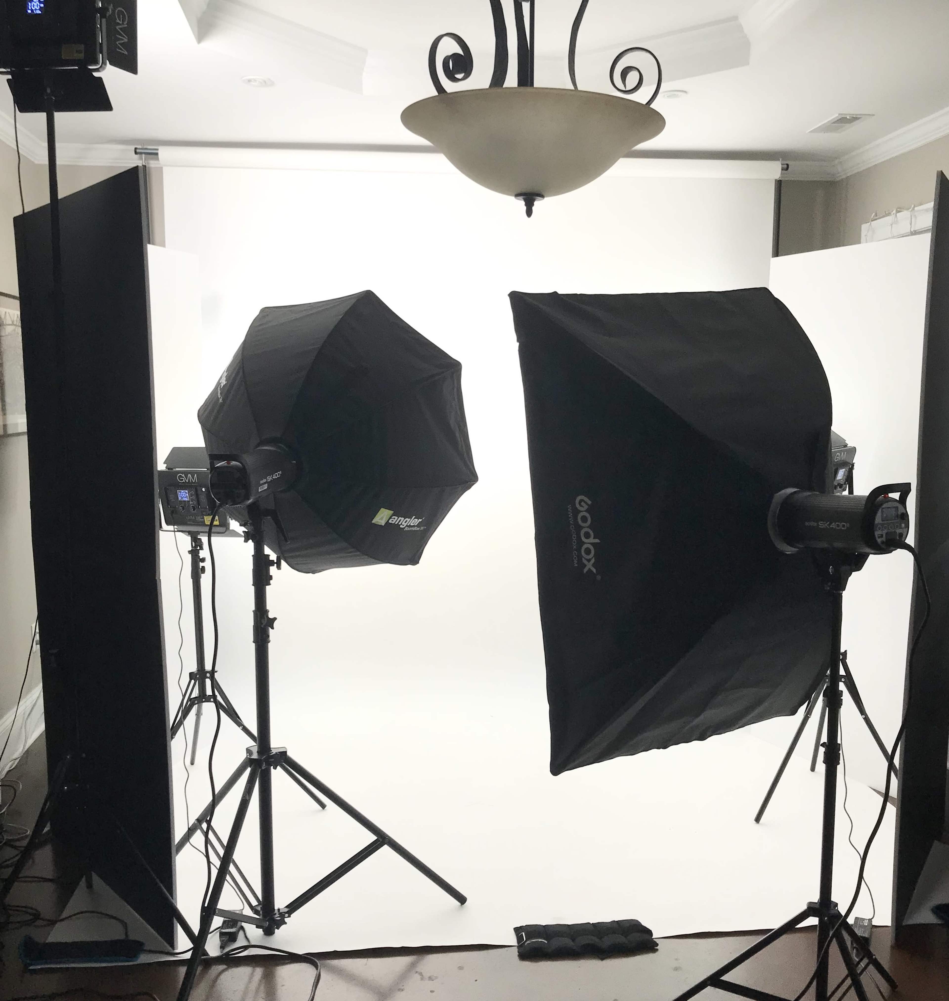 A photography setup with two softbox lights positioned on either side of a white backdrop in a studio setting.