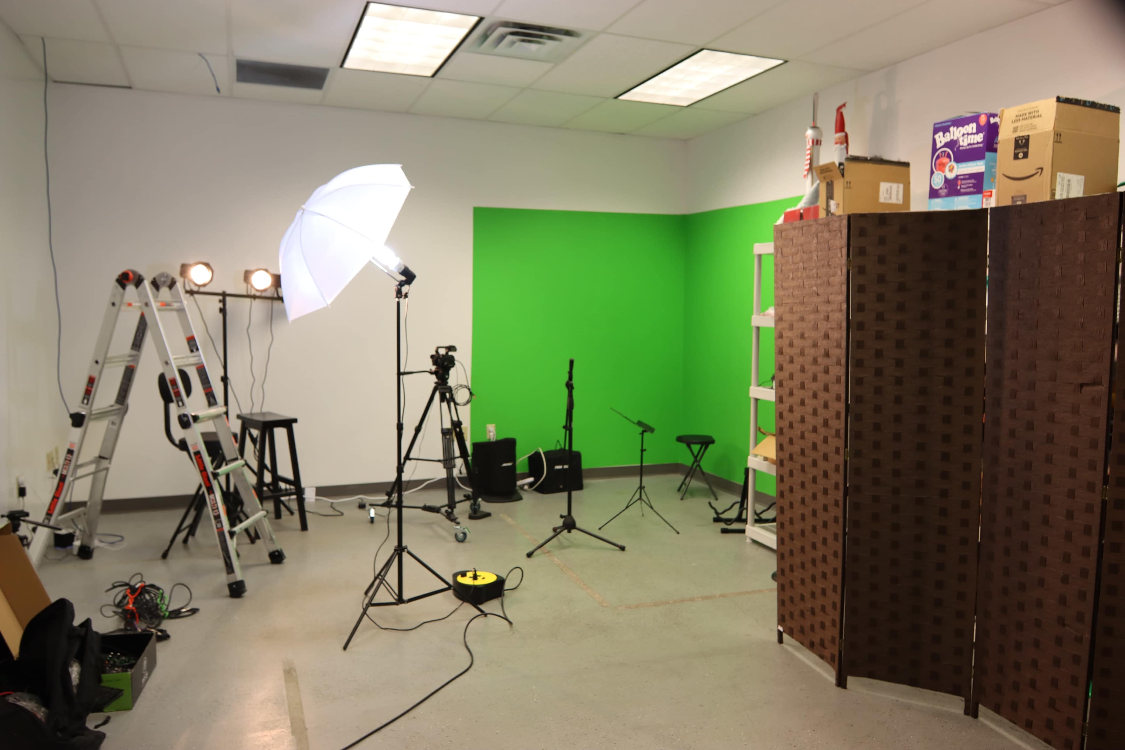 A studio space with lighting equipment, a green screen wall, musical instruments, and a folding room divider.