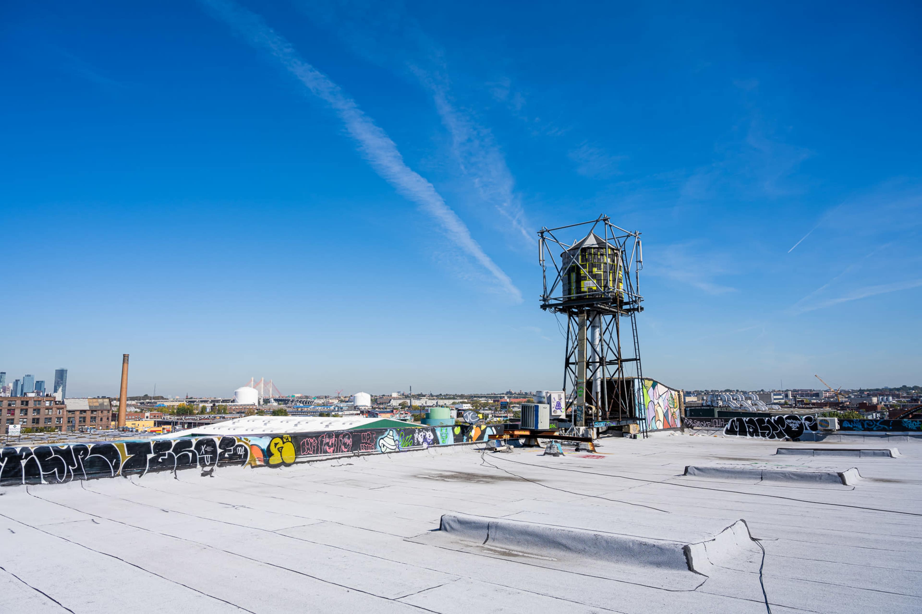 The image shows a rooftop view with a water tower and graffiti adorned surfaces against a clear blue sky.
