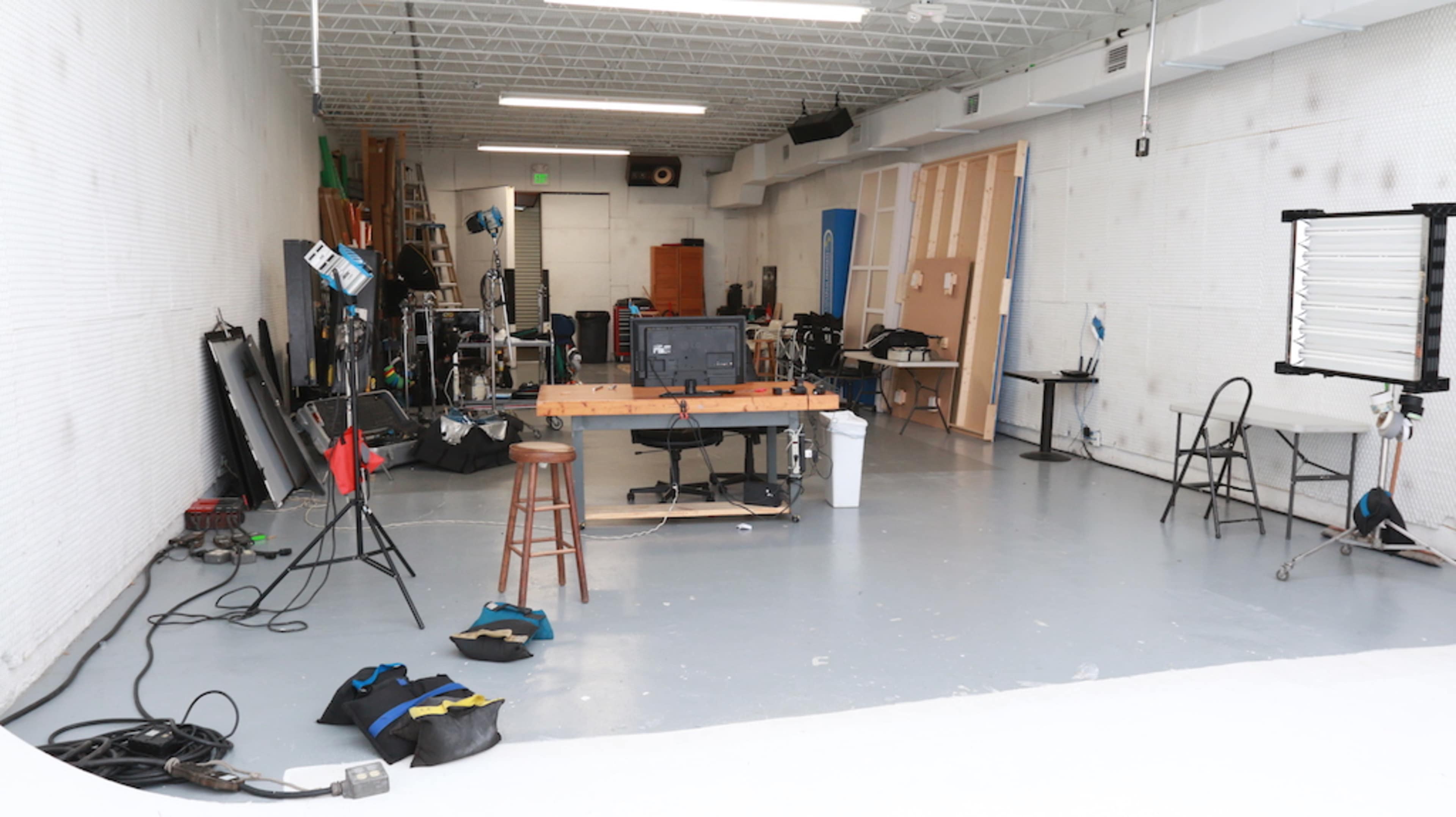 The image shows a photography studio with various equipment, including lighting stands and a work table, arranged in a spacious environment.