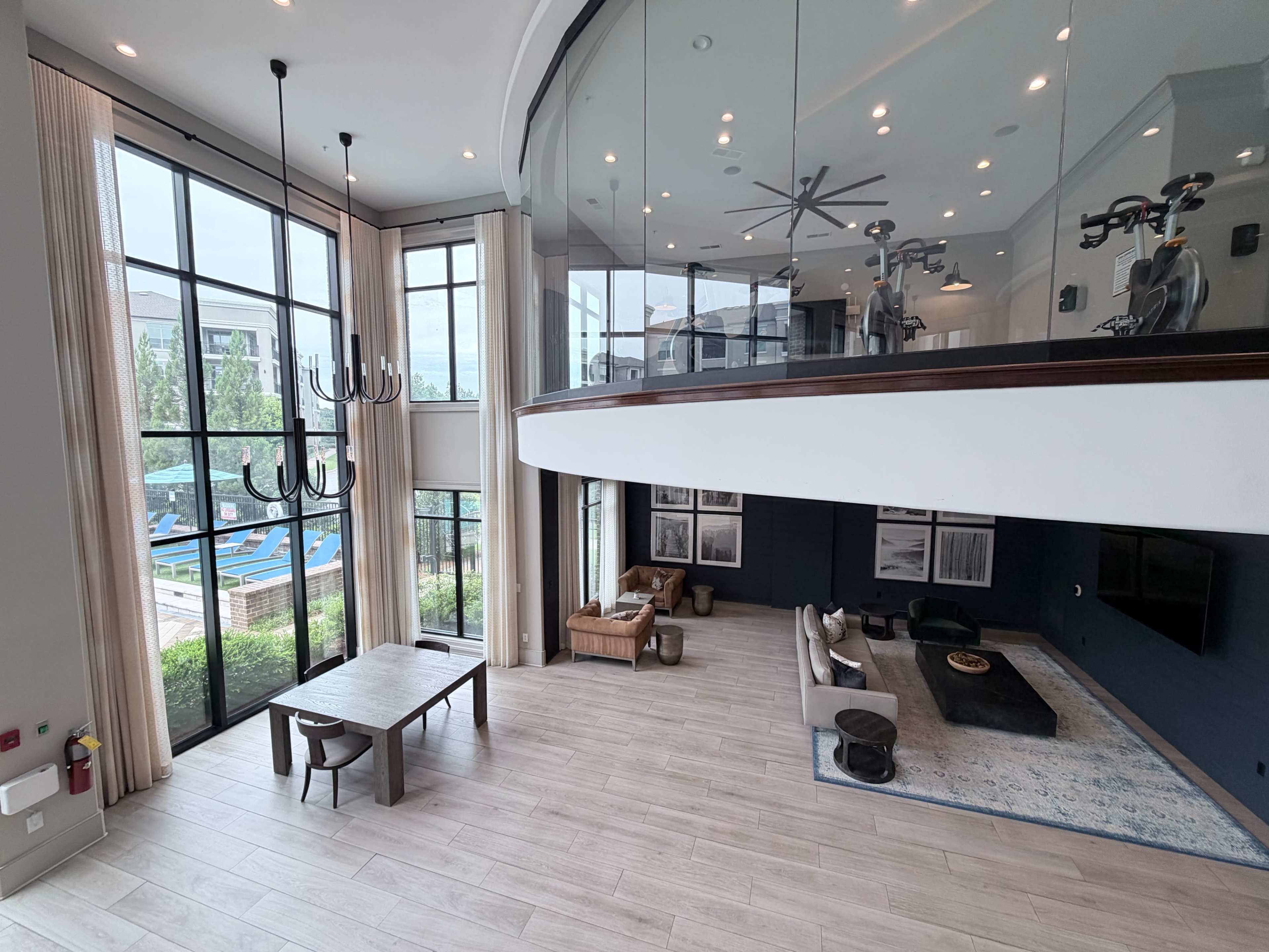 The image shows a modern, open-concept living space with large windows, a dining table, and a lounge area featuring a sofa and a coffee table.