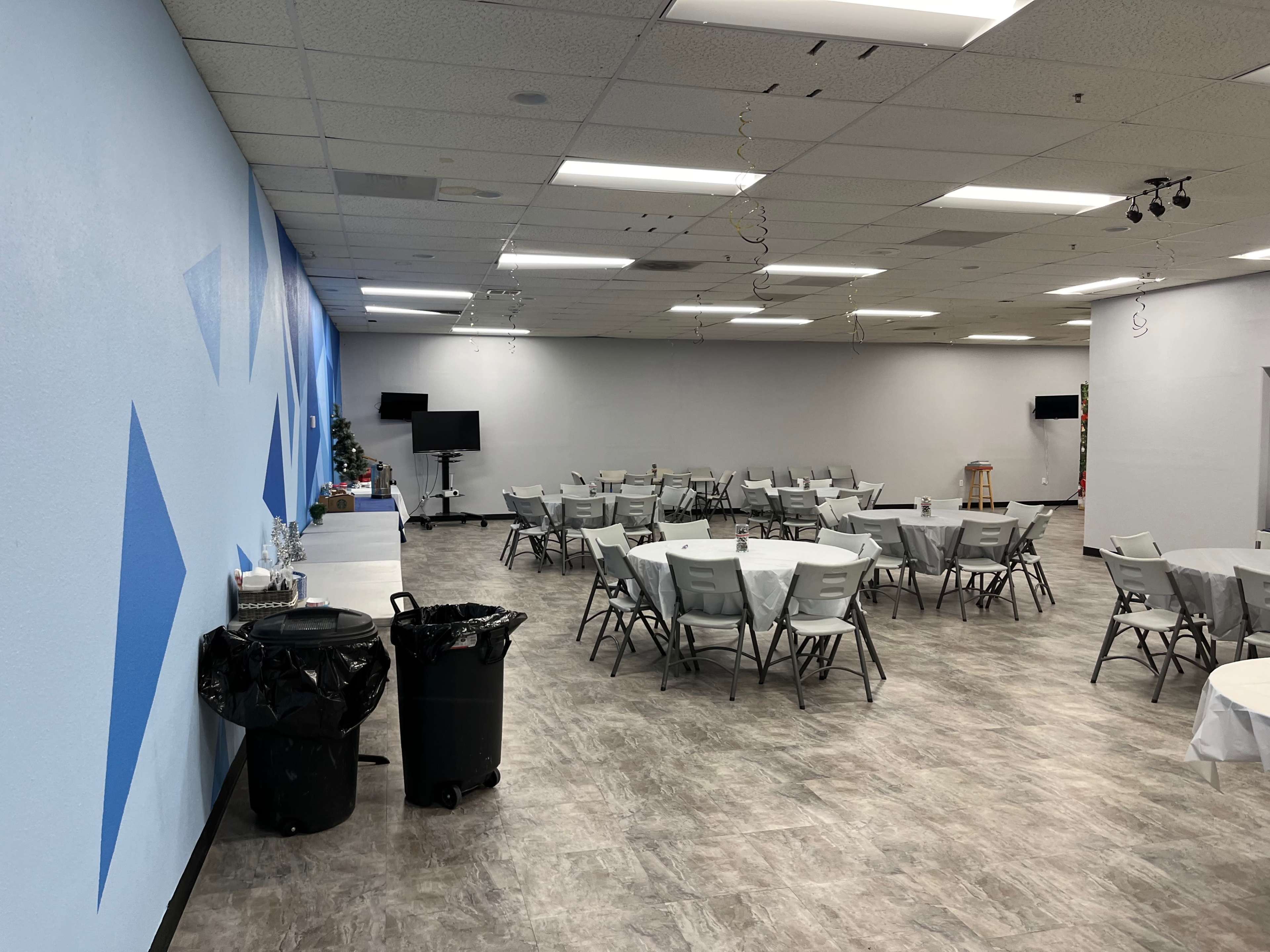 A large room with gray flooring, multiple tables set with white tablecloths, and blue painted walls featuring geometric designs.