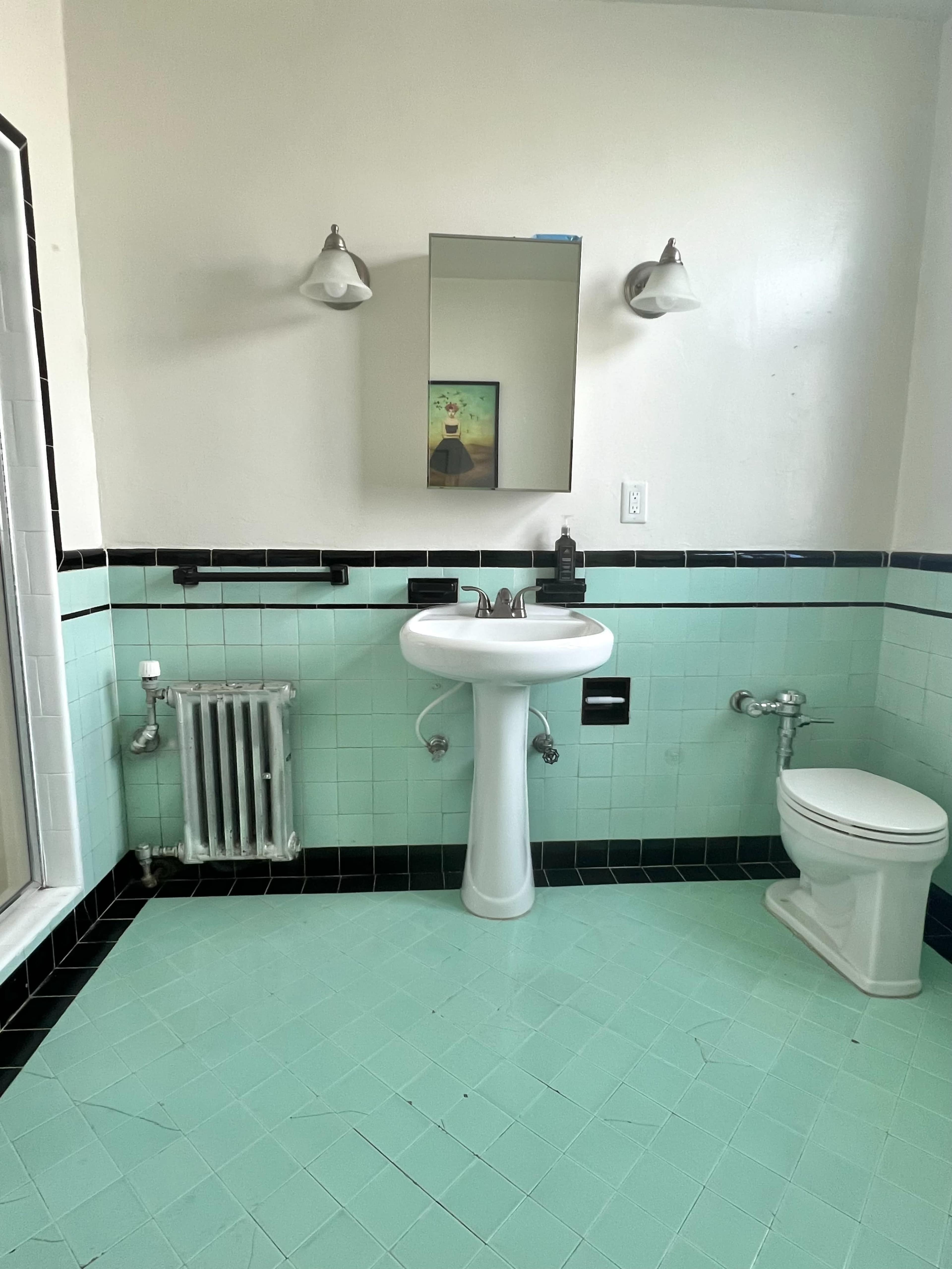 The image shows a bathroom with mint green tiled walls, a pedestal sink, a toilet, and a mirror above the sink.