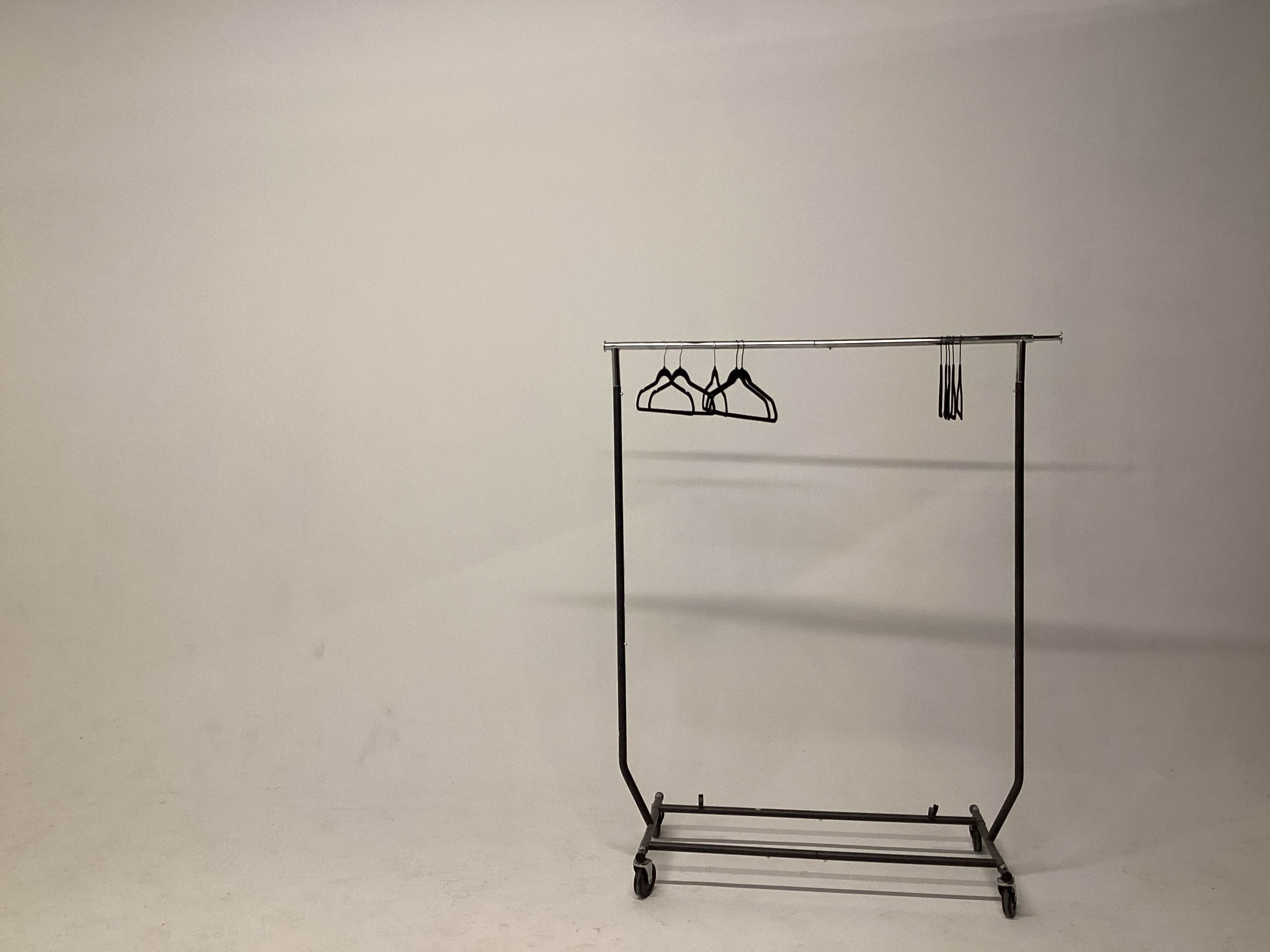 A clothing rack with several hangers stands in front of a plain white background.
