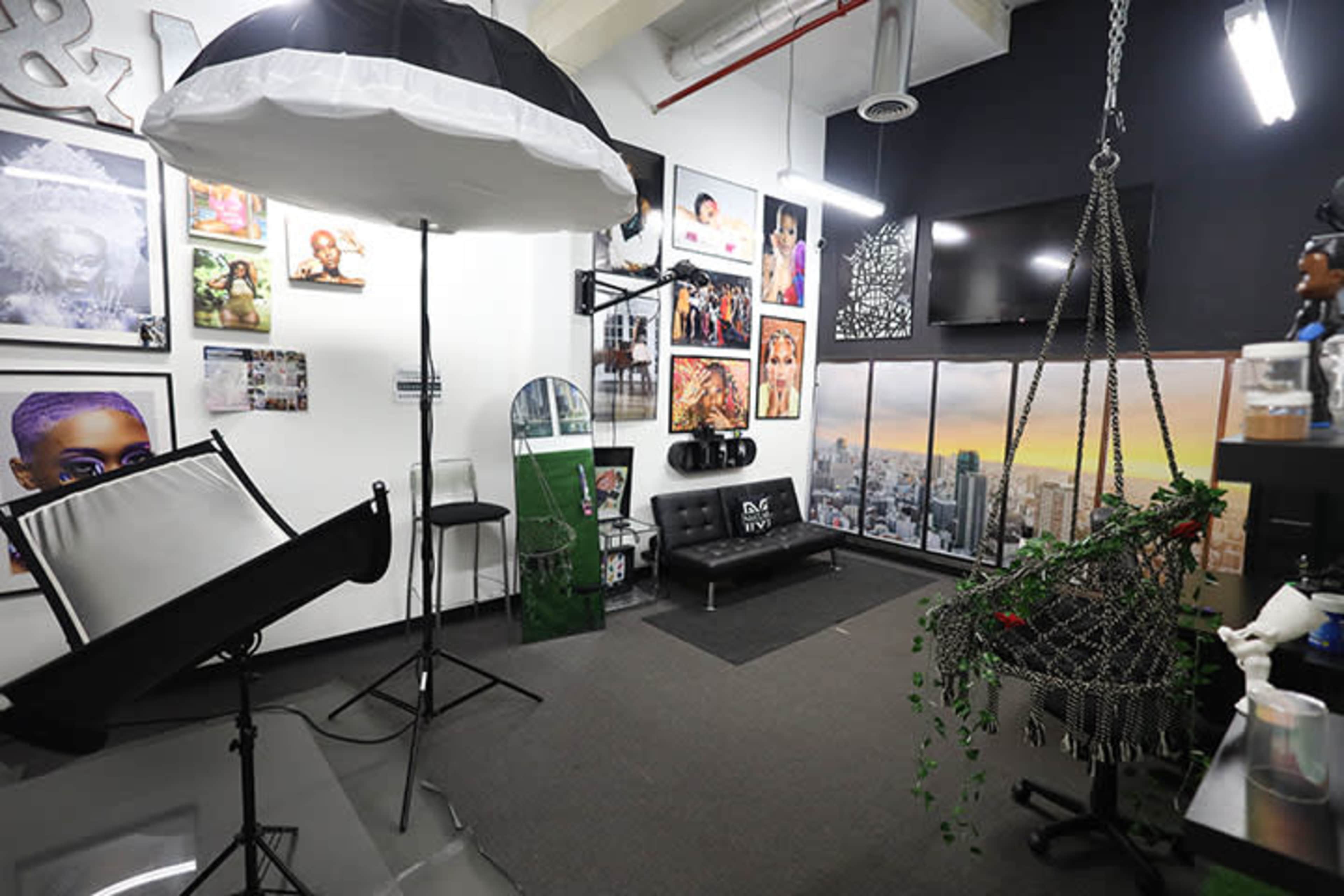 The image shows a photography studio featuring various framed portraits on the walls, a swing chair decorated with plants, and professional lighting equipment set up for shoots.