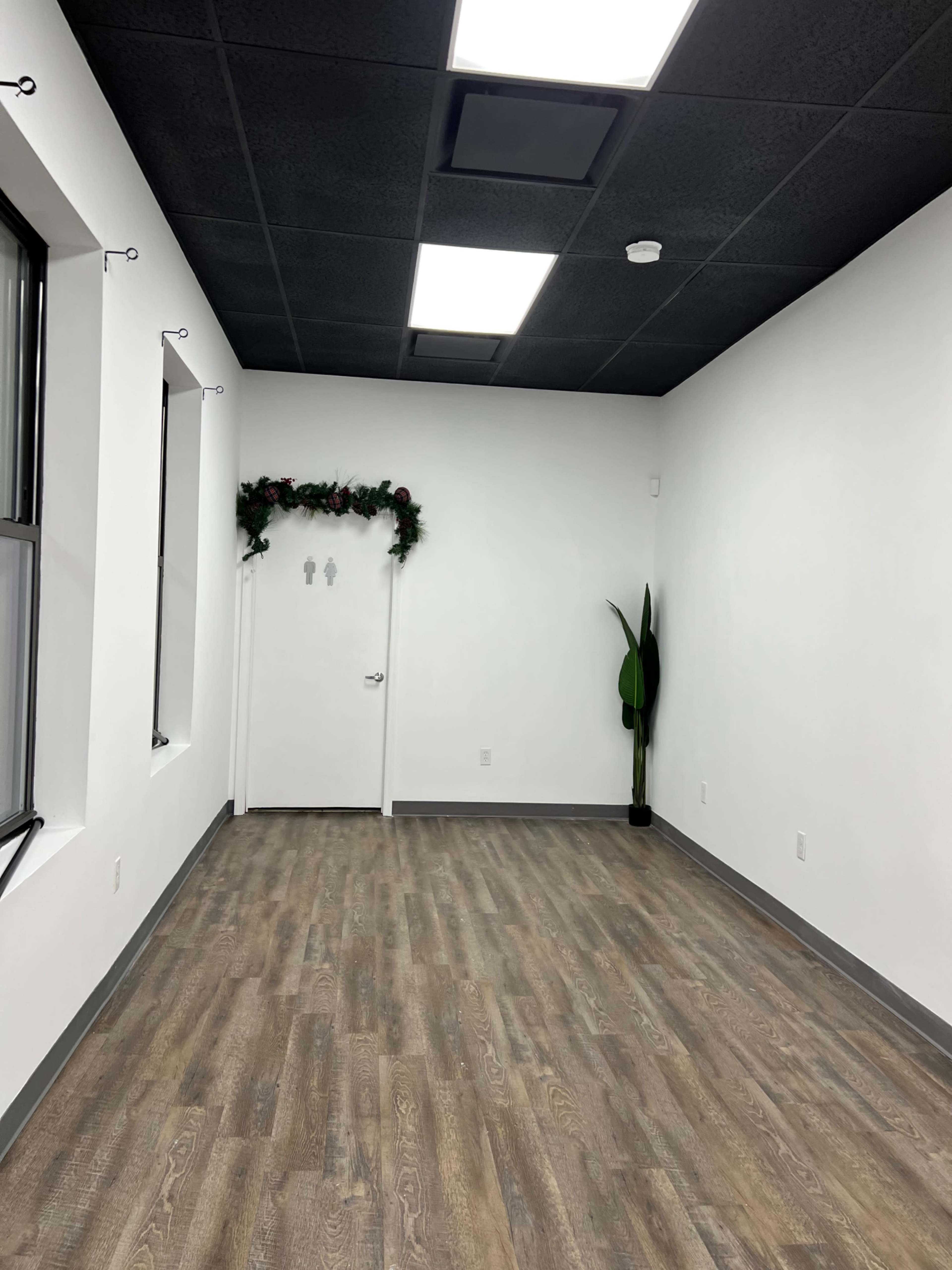 A sparse room with a wooden floor, white walls, and a door adorned with holiday greenery.