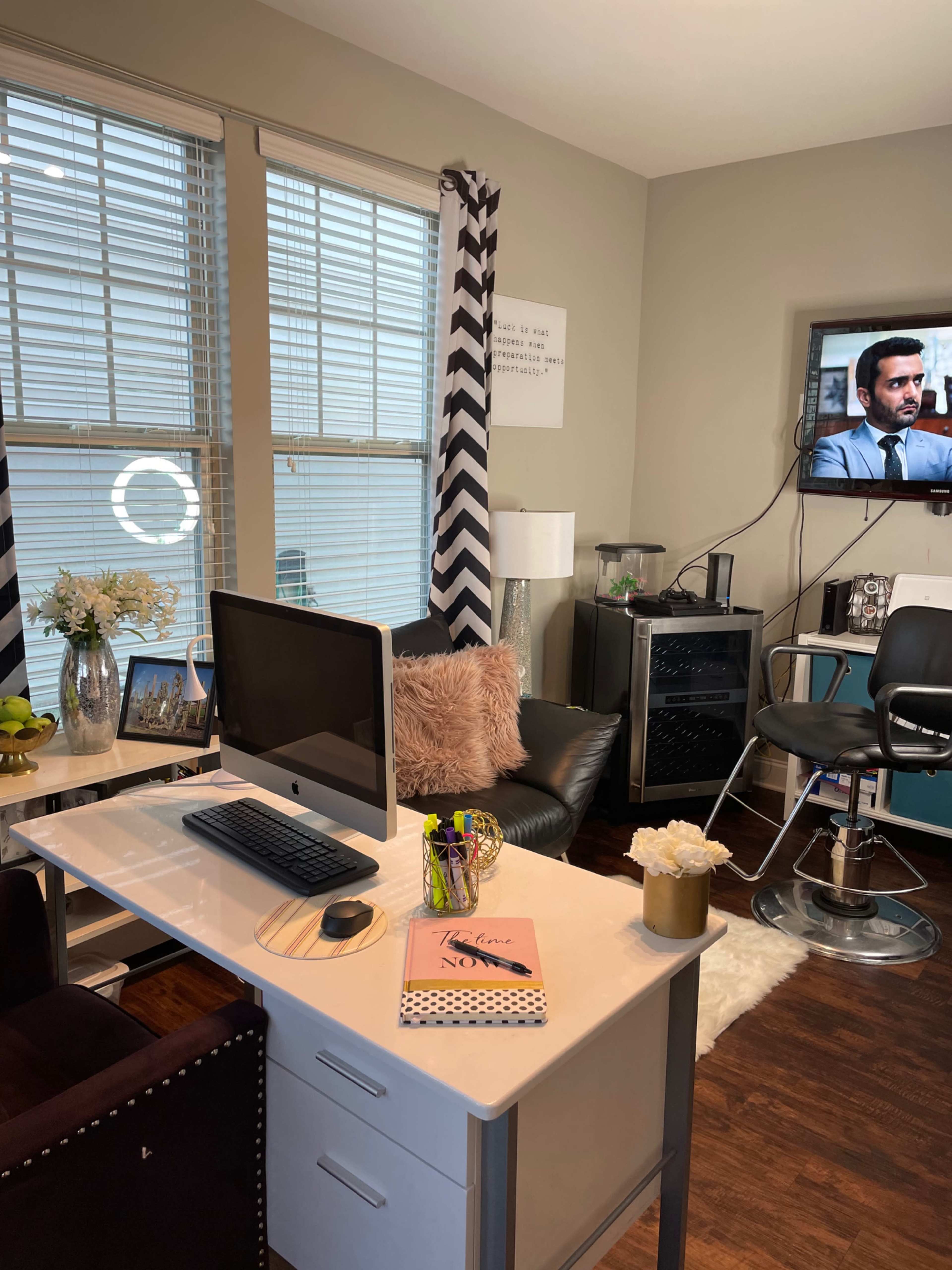 A small office space with a desk, computer, and a TV, featuring black and white striped curtains and a leather chair.