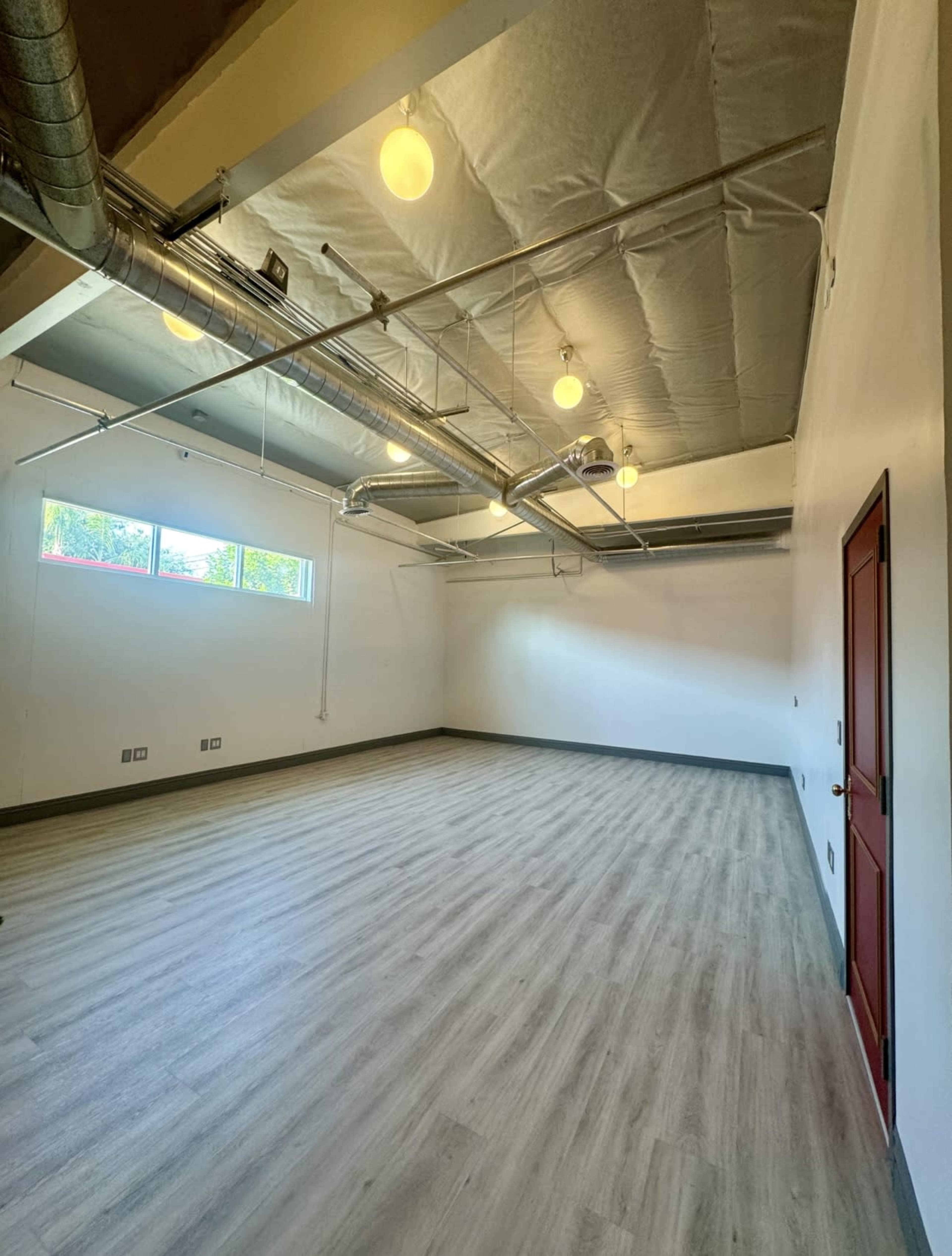 An empty room with a wooden floor, exposed ductwork, and several hanging light fixtures.