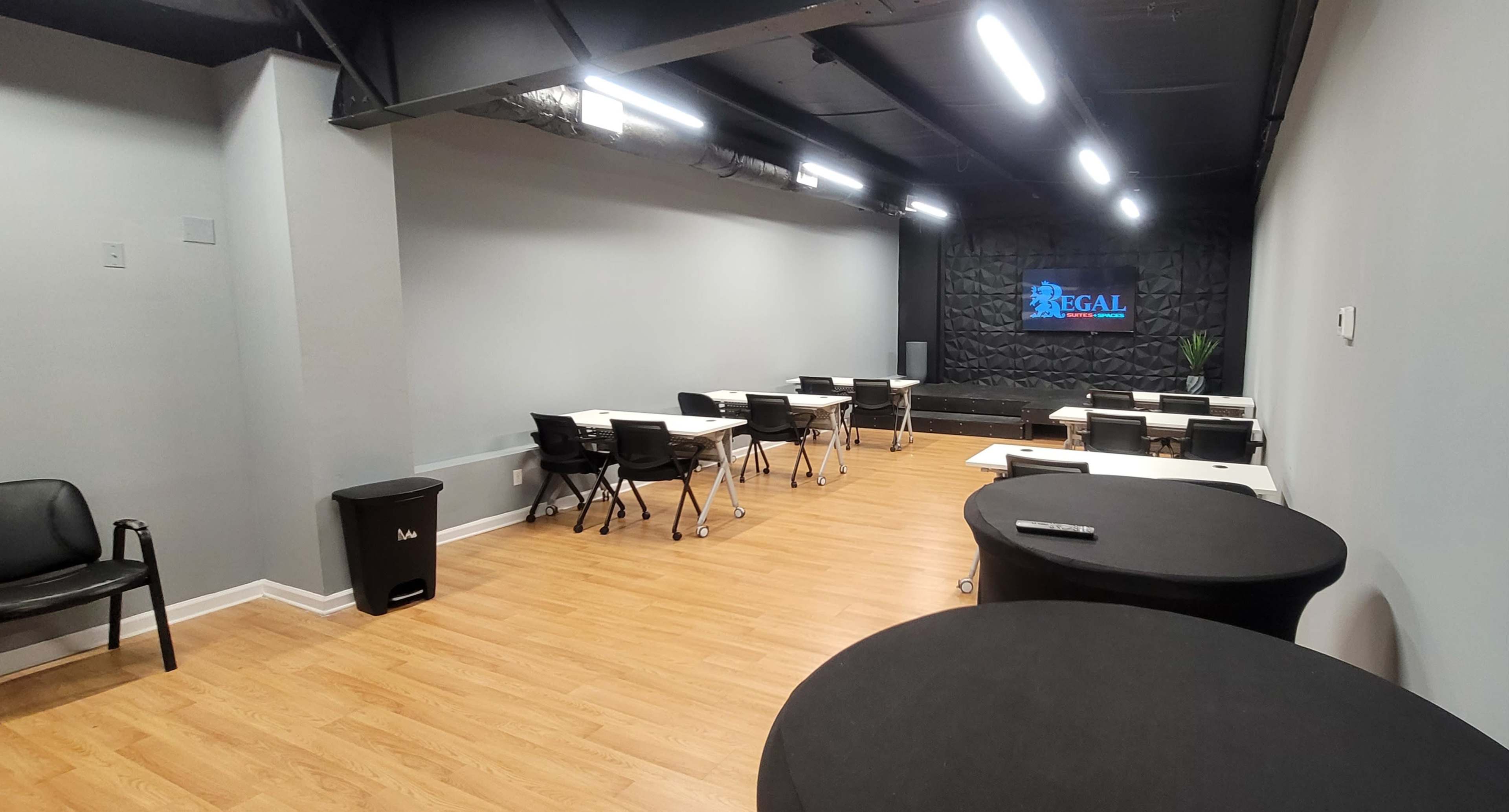 A modern, empty meeting room featuring several tables and chairs, with a black wall displaying a "REGAL" sign.