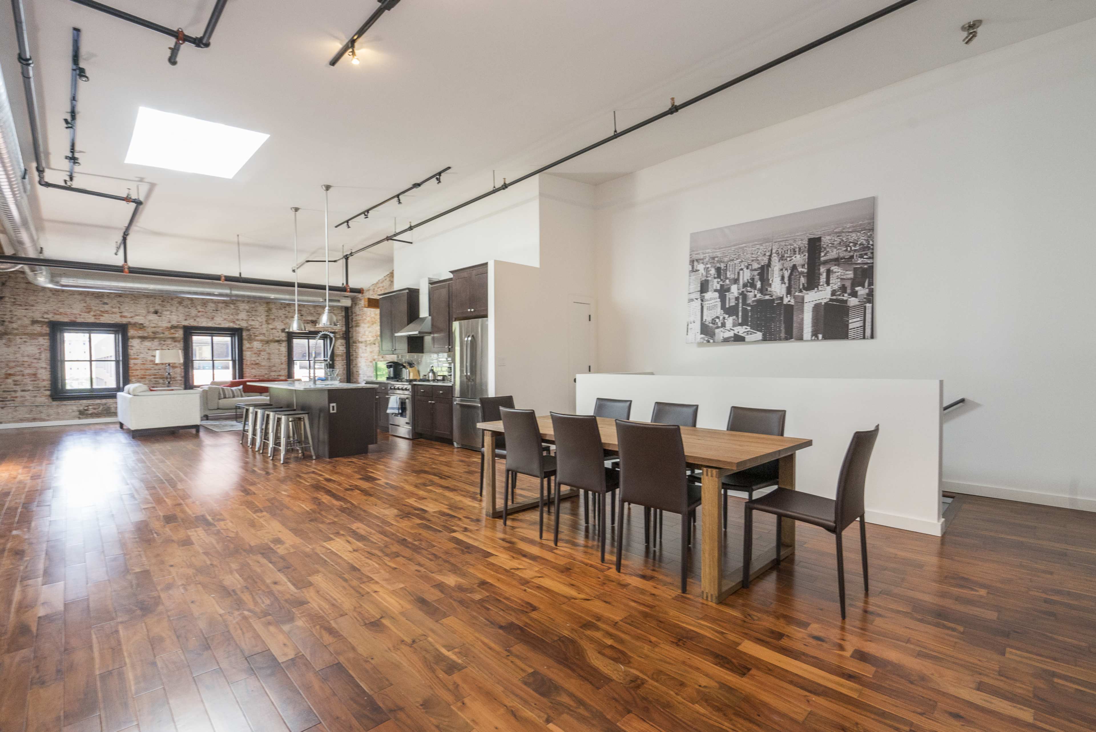 An open-concept loft with exposed brick walls, a modern kitchen, and a large dining table set for six.