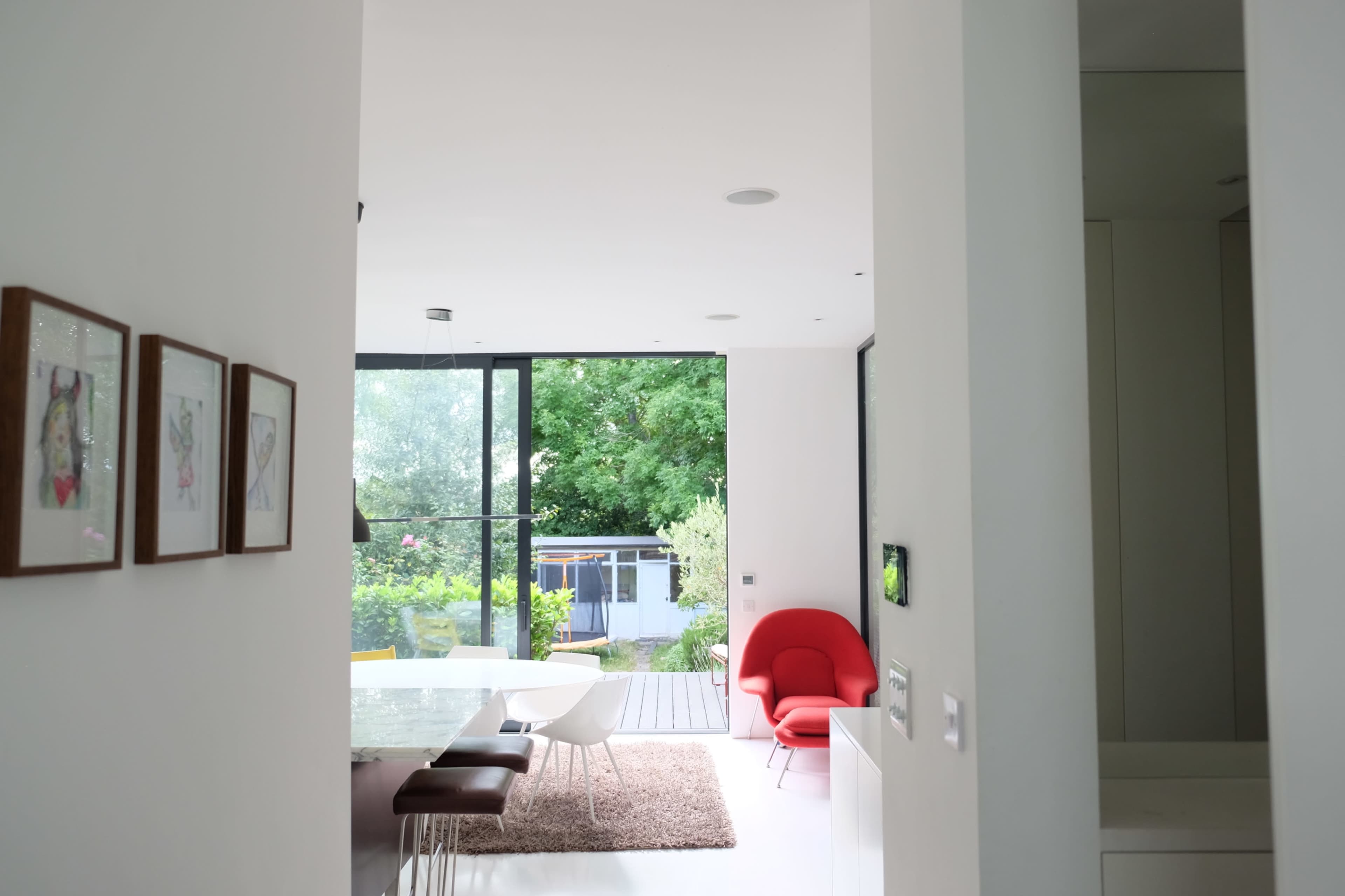A modern interior hallway leading to an open living space with a dining area and large windows overlooking a garden.