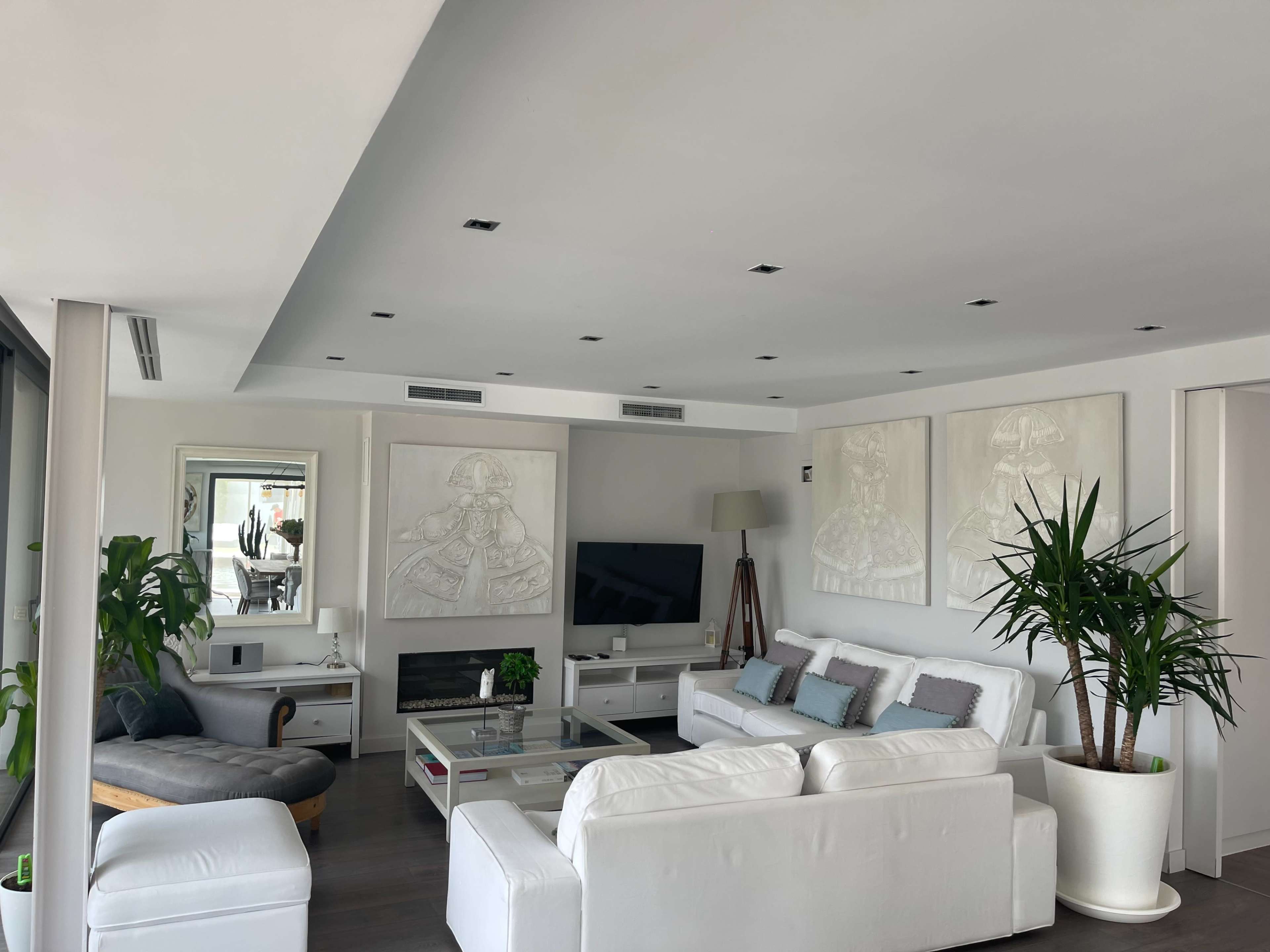 A modern living room features white furniture, two large wall art pieces, and a television mounted above a fireplace.