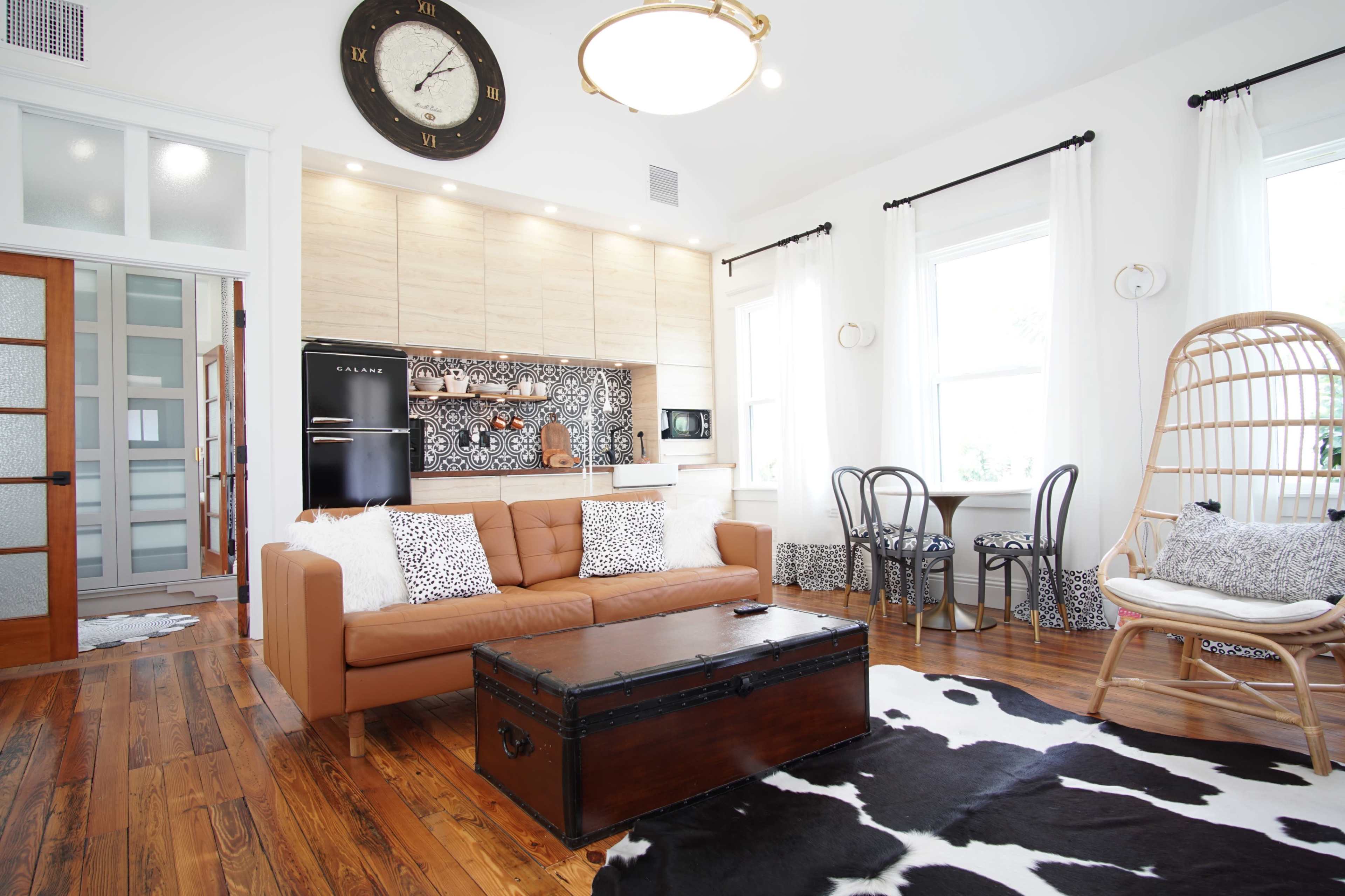 A modern living area featuring a brown couch, a wooden coffee table, a black refrigerator, and a dining set, all complemented by light-colored walls and a cowhide rug.