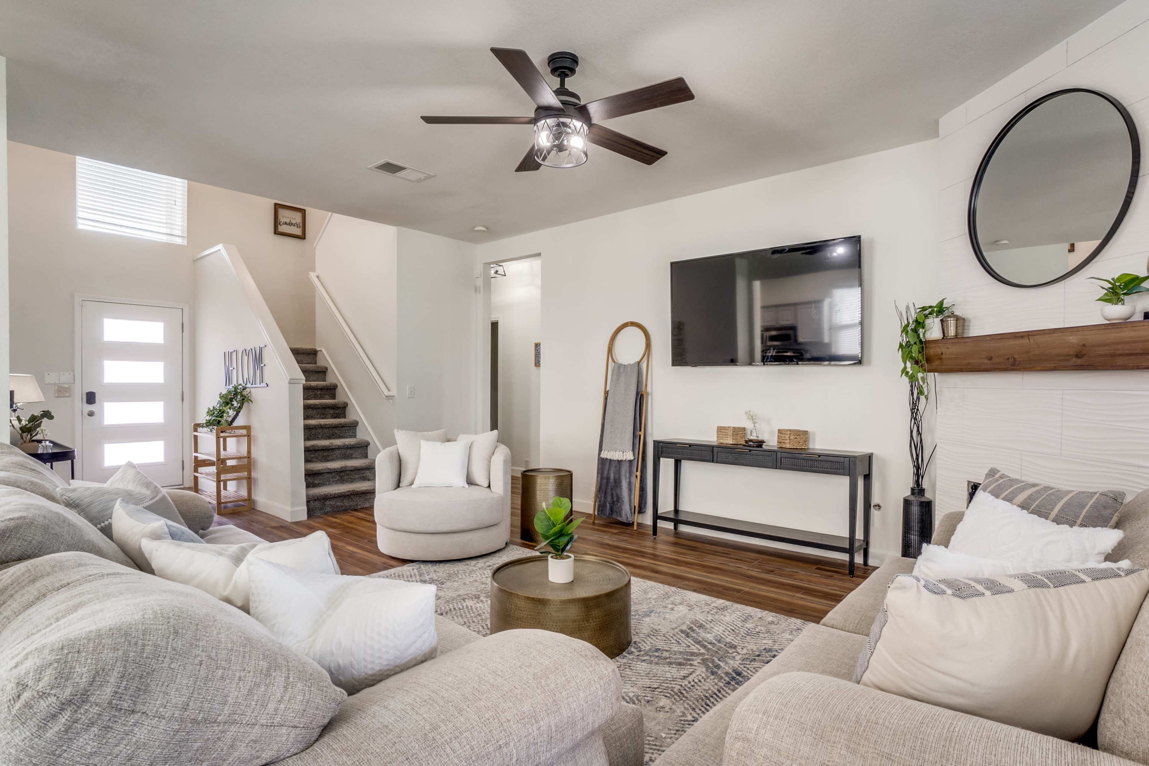 A modern living room featuring a sectional sofa, a circular chair, a coffee table, a wall-mounted television, and a staircase in the background.