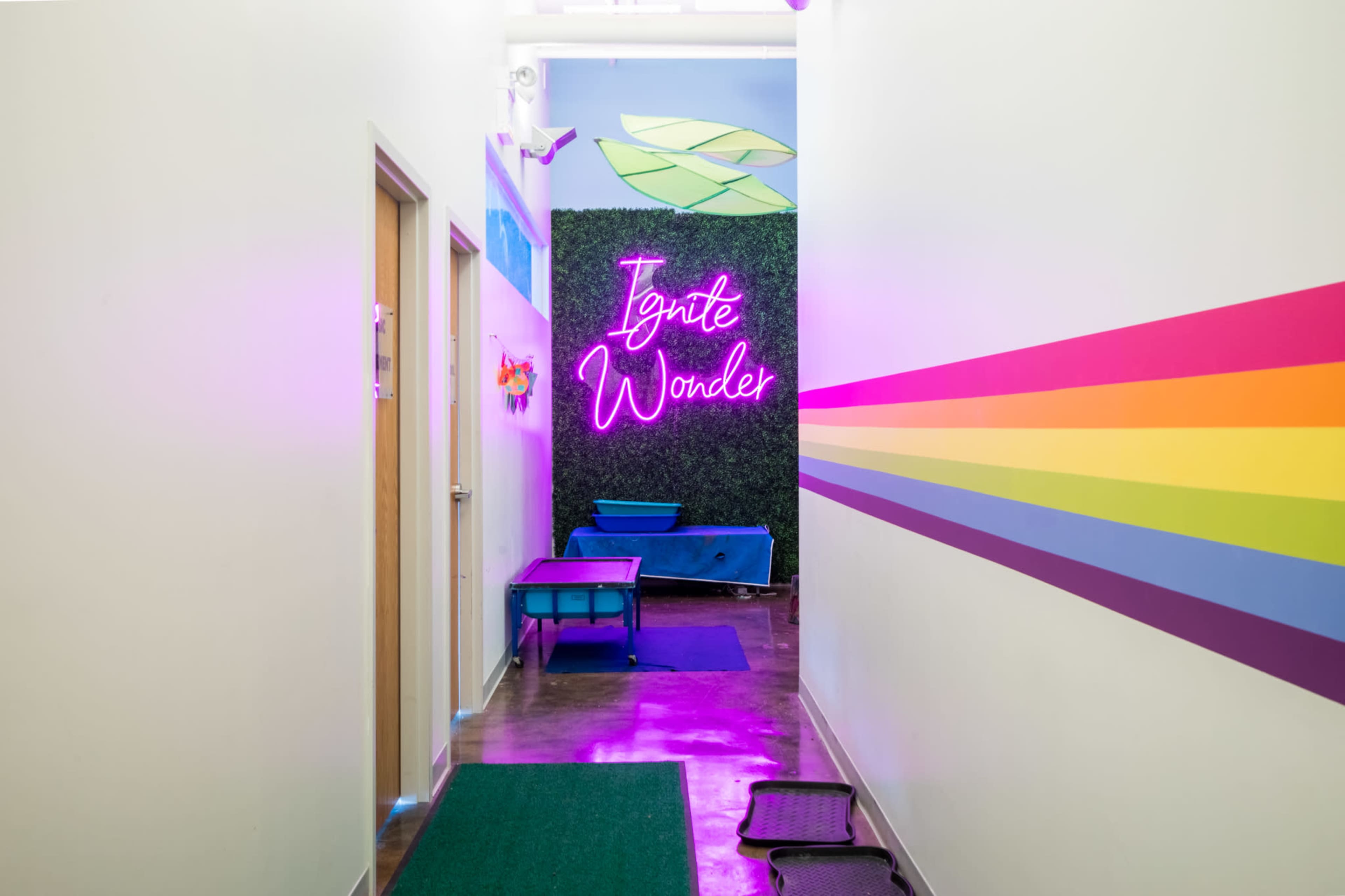 A brightly colored hallway features a neon sign that reads "Ignite Wonder," flanked by vibrant rainbow stripes and green accents.