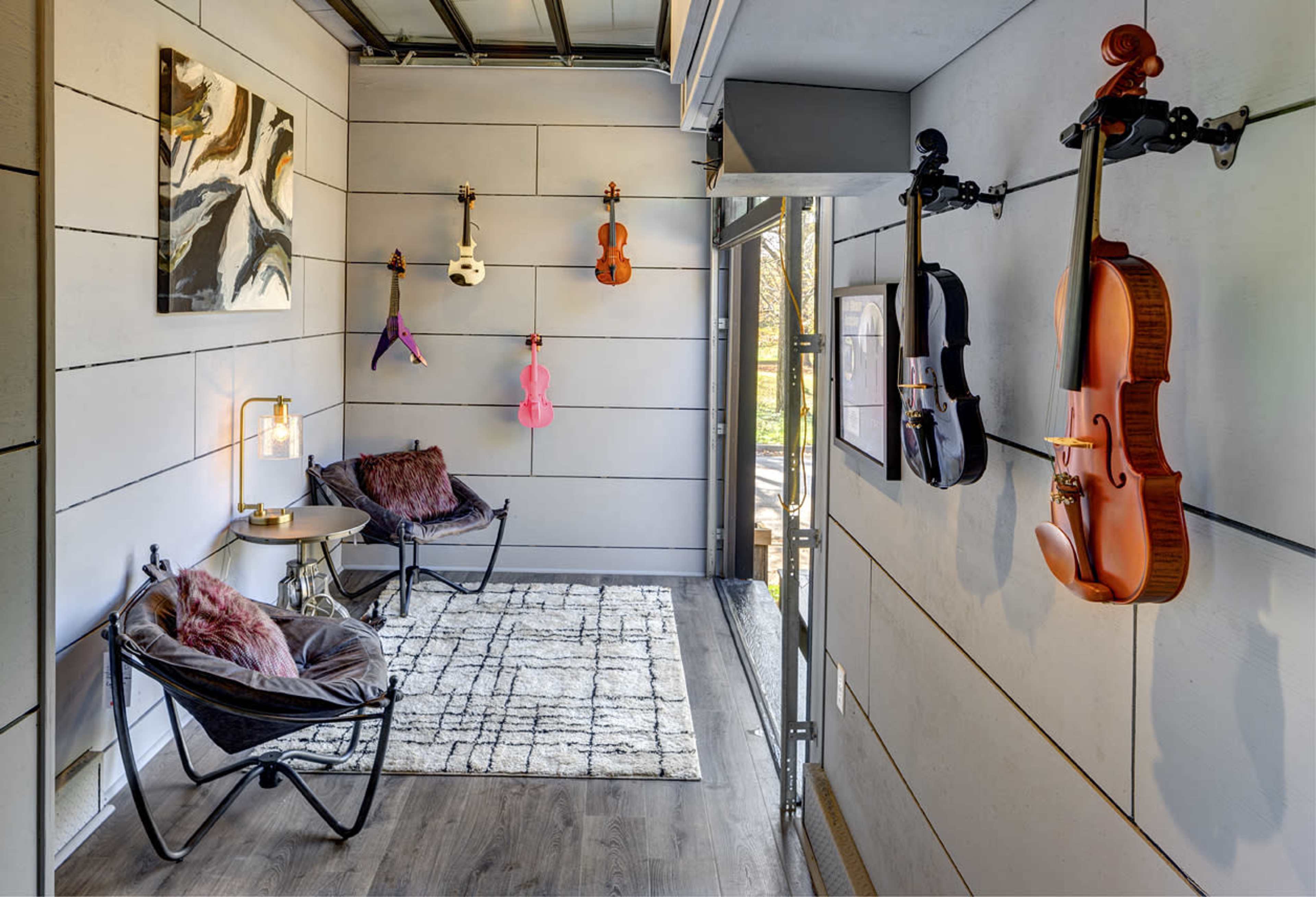 A modern room featuring several violins displayed on the walls, along with a small seating area and a decorative rug on the floor.