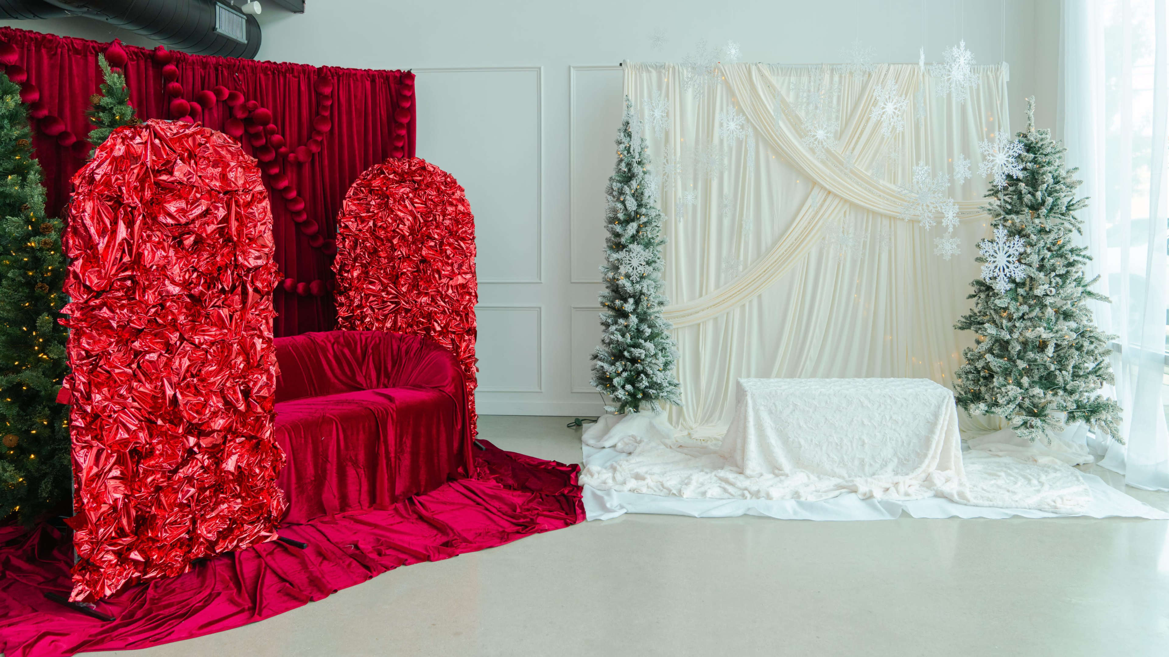 The image shows a festive indoor space featuring a red seating area with ornate fabric backdrops and two decorated Christmas trees on either side.