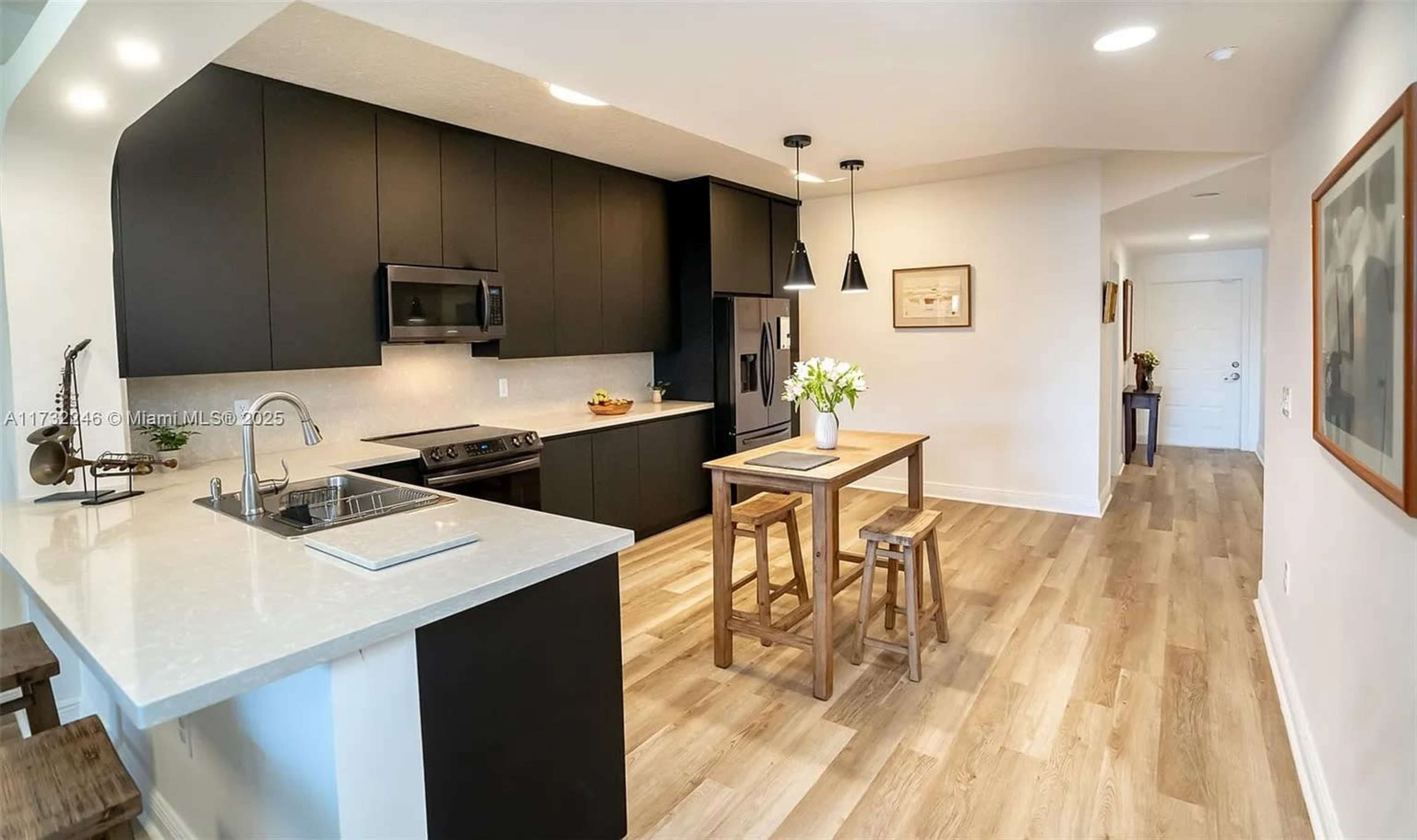 The image shows a modern kitchen with black cabinetry, a stainless steel stove, and a small dining table with wooden stools.