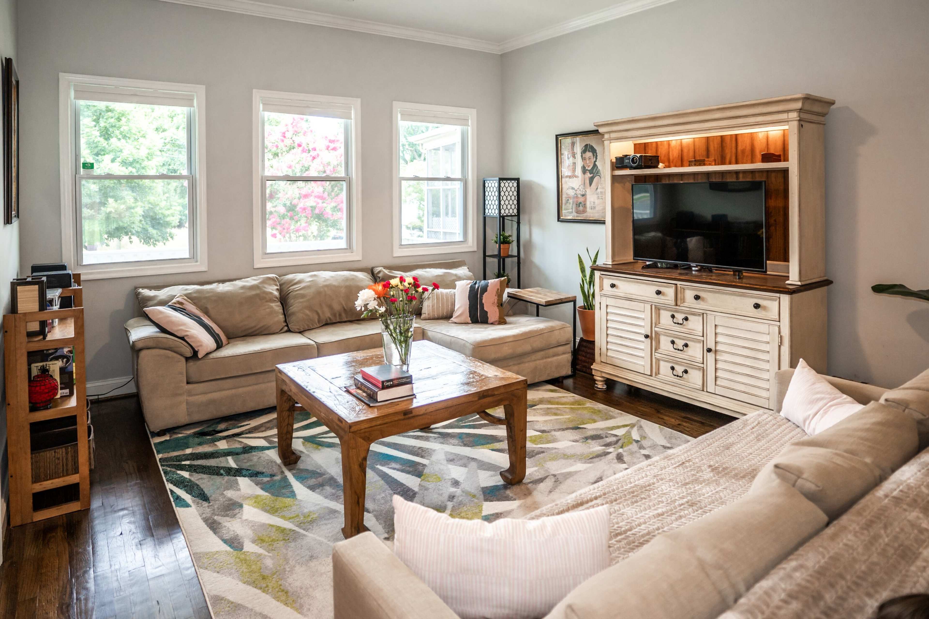 The living room features a beige sectional sofa, a wooden coffee table, and a media console with a television, all arranged around a patterned area rug.