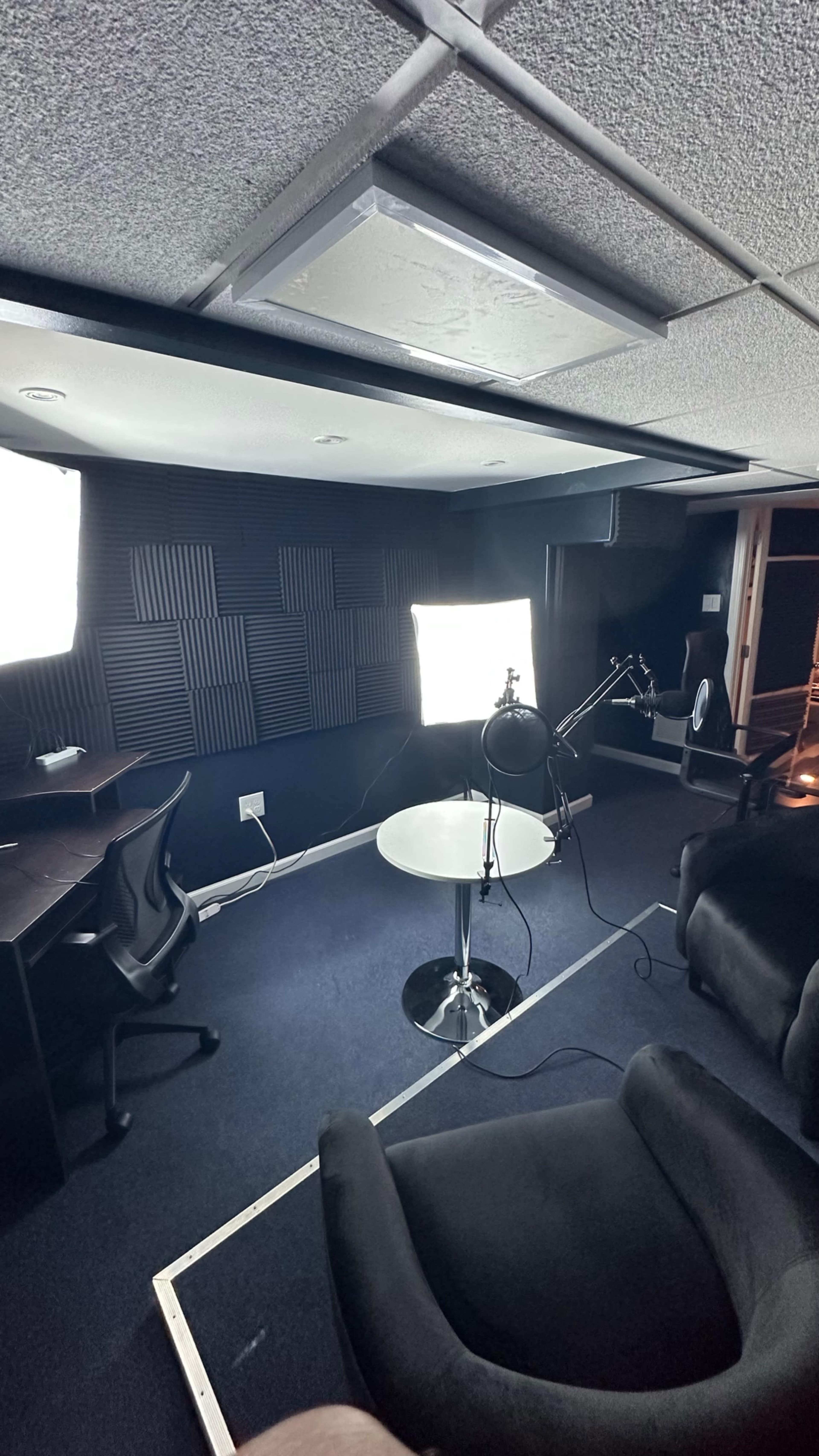 A recording studio with a microphone setup, two soft chairs, and bright lighting.