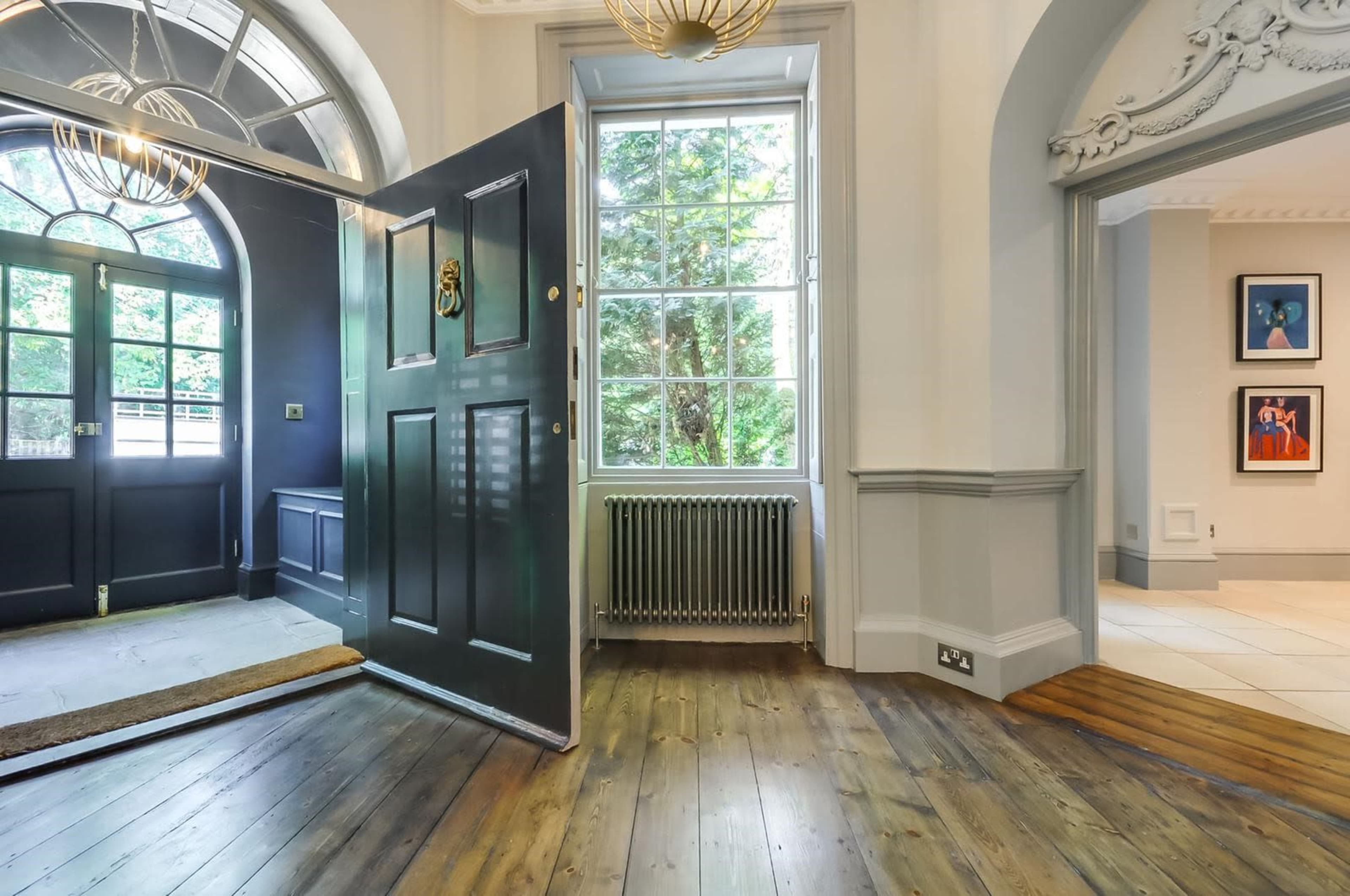 An open front door leading into a room with hardwood flooring, large windows, and a radiator.