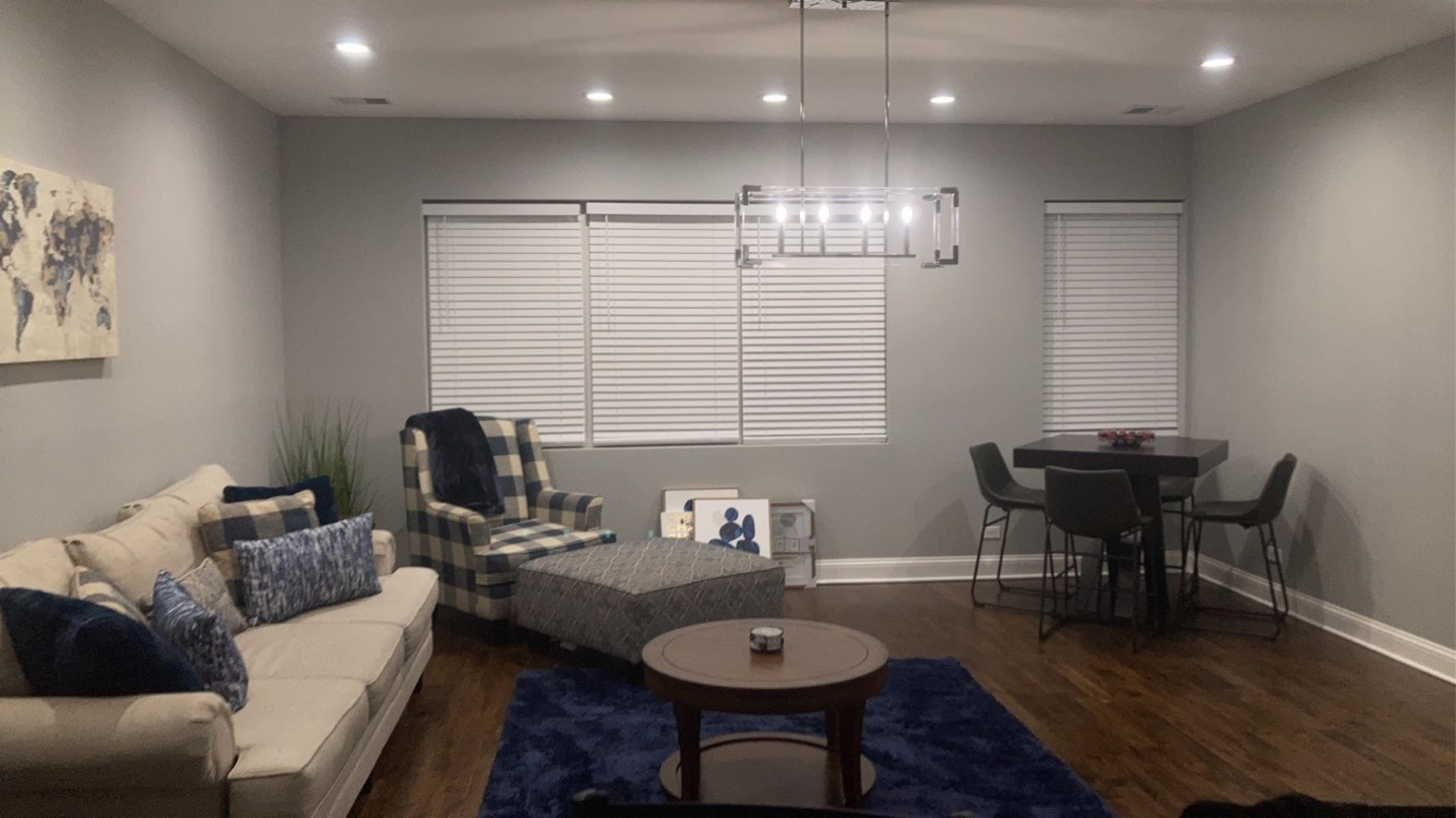 A modern living room with a sofa, a plaid armchair, a round coffee table, and a dining space with four chairs.
