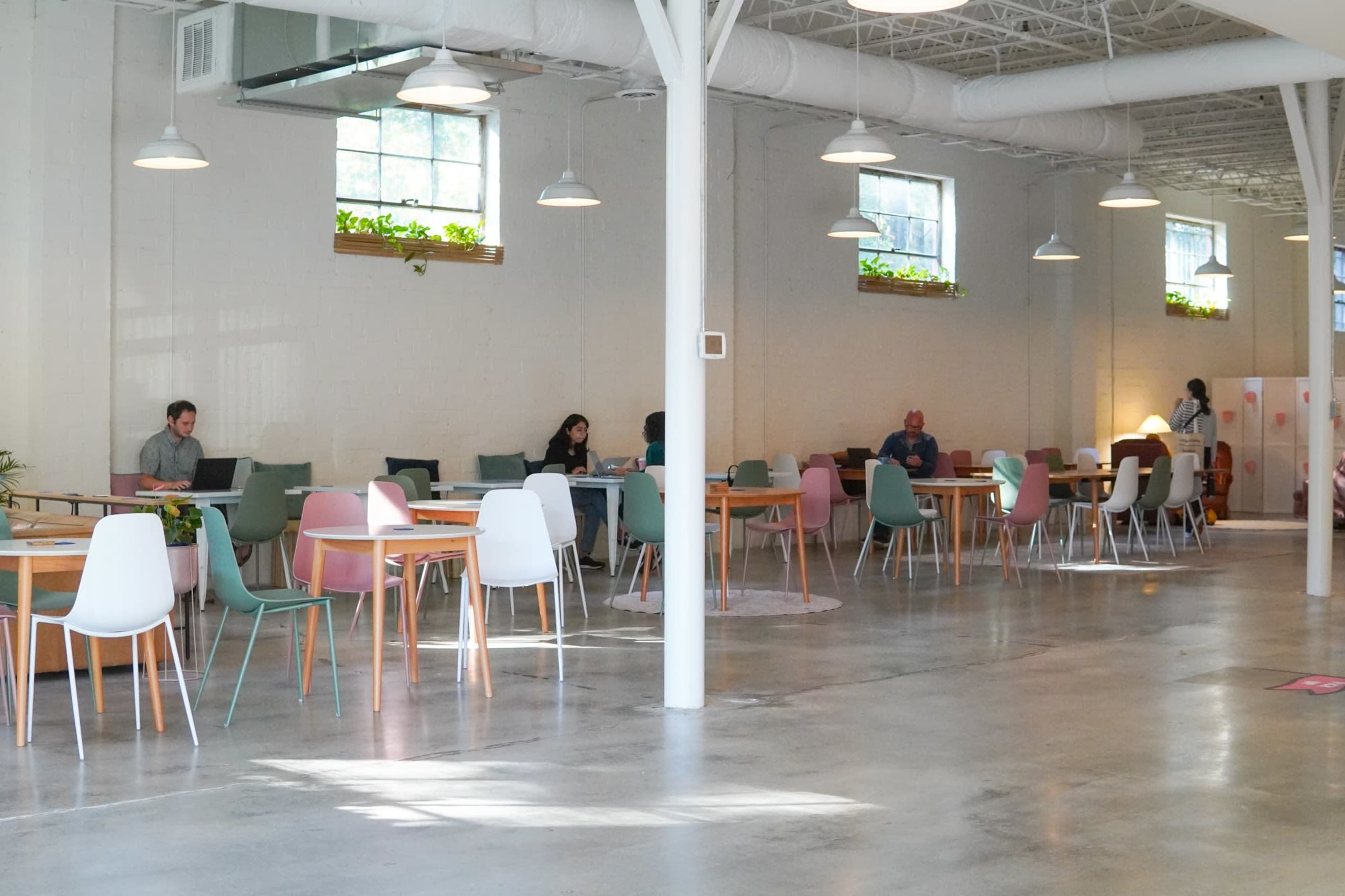 The image shows a spacious, well-lit interior of a café or co-working space with several tables and people working at them.