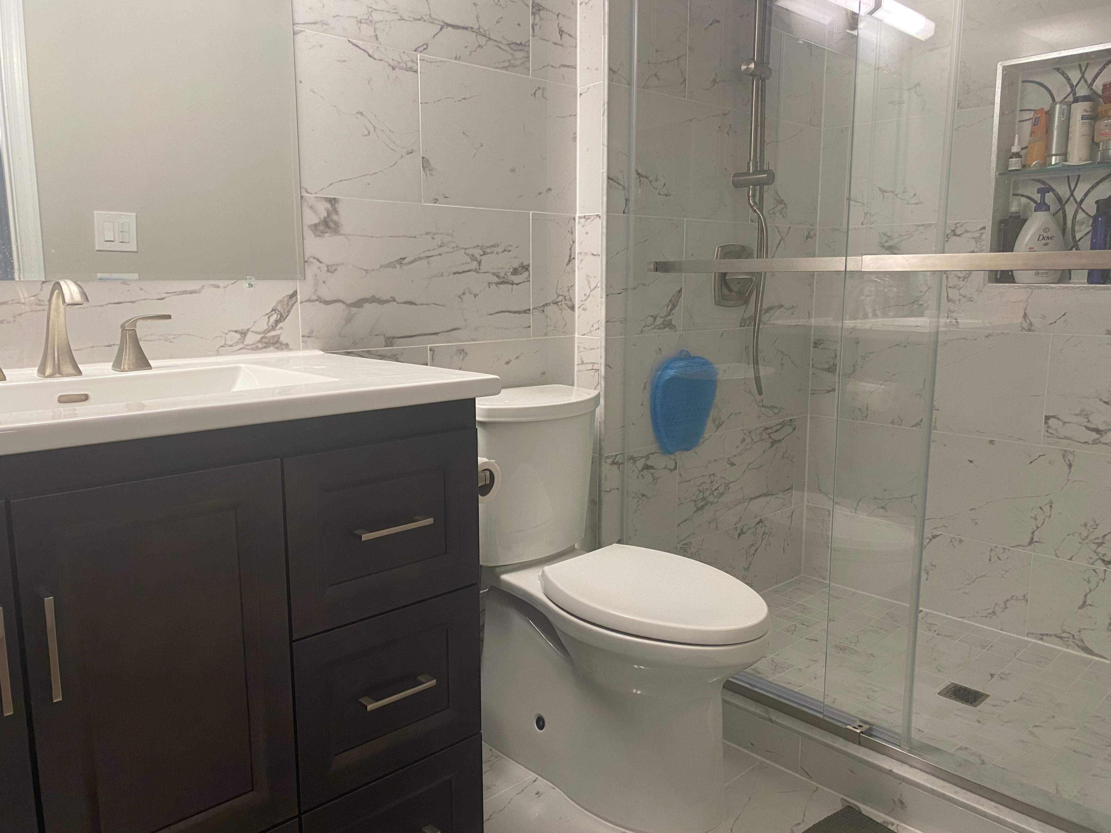 A modern bathroom featuring a white vanity with a sink, a toilet, and a glass-enclosed shower with marble-patterned tiles.