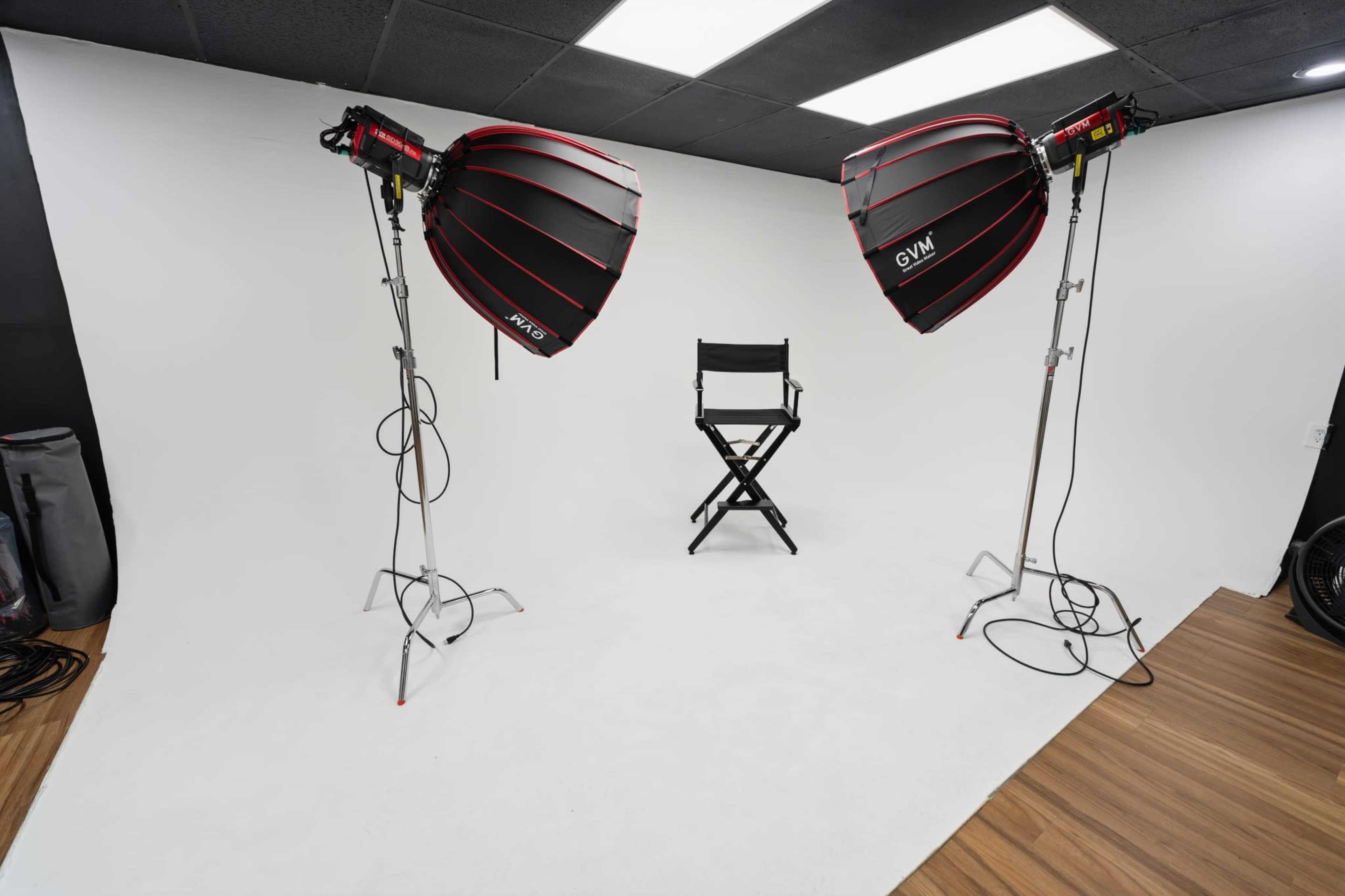 The image depicts a photography studio featuring two large softbox lights and a director's chair positioned in front of a white backdrop.