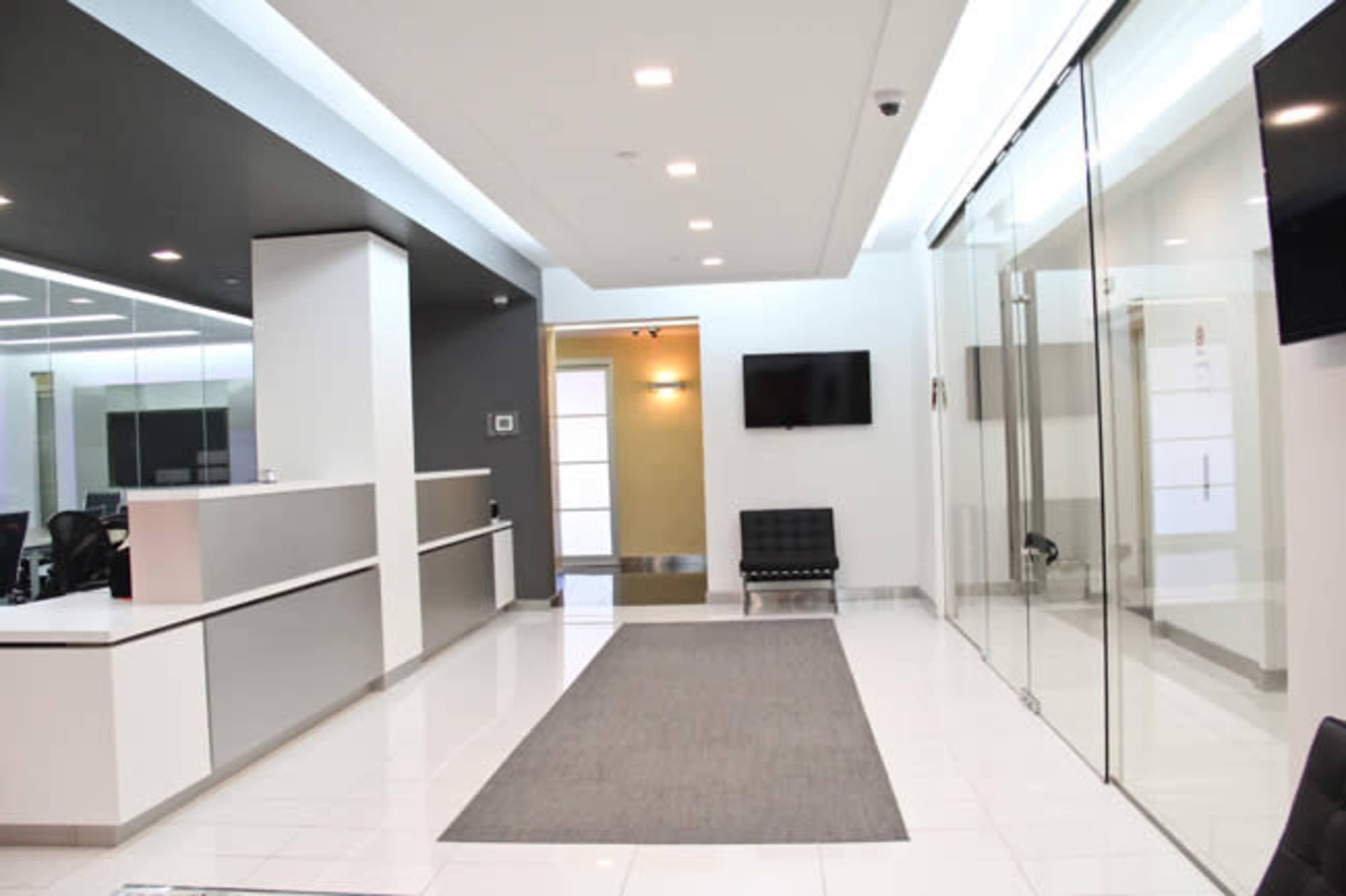 A modern office reception area featuring a sleek front desk, glass walls, and a gray carpet.